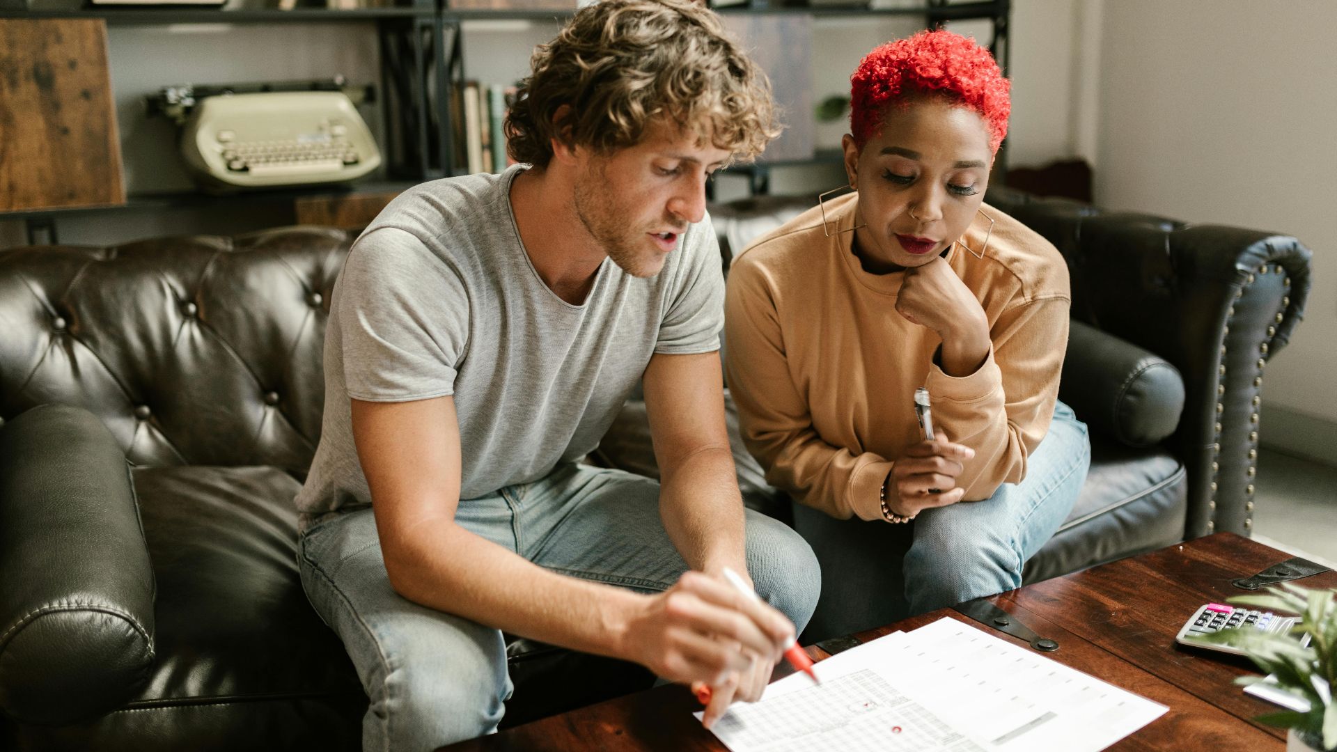 A couple sitting on a sofa examines documents in a cozy, modern living room setting.