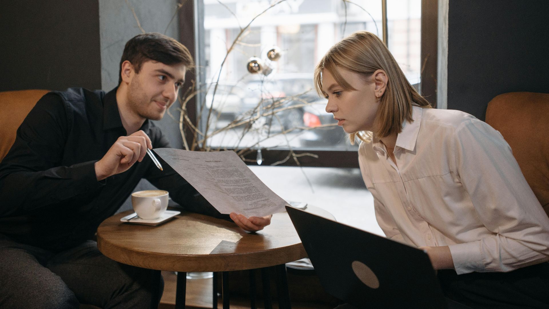 Engaged colleagues discussing documents over coffee in a cozy cafe setting.