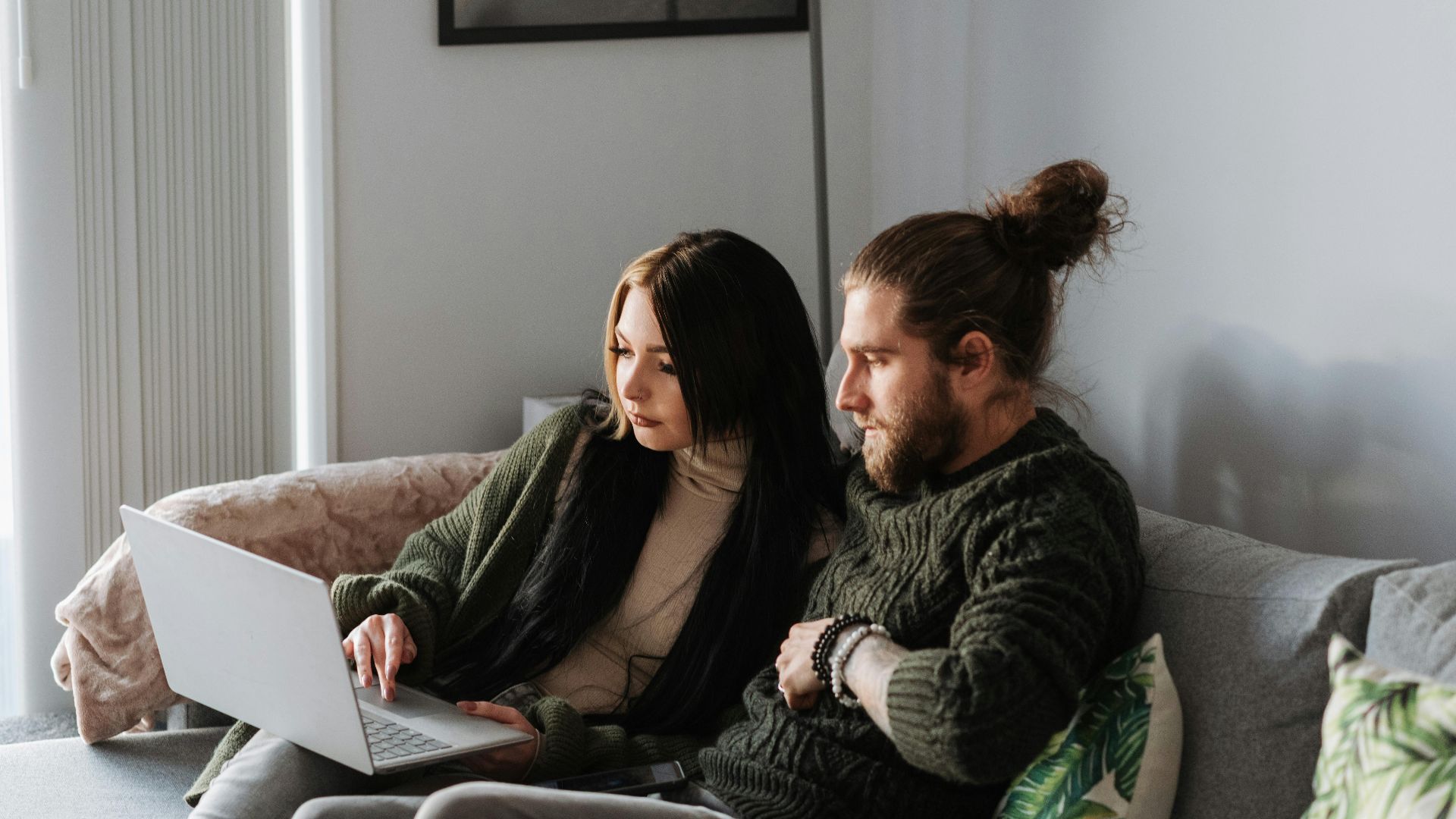 A young couple enjoys a relaxing day at home using their laptop on the couch.