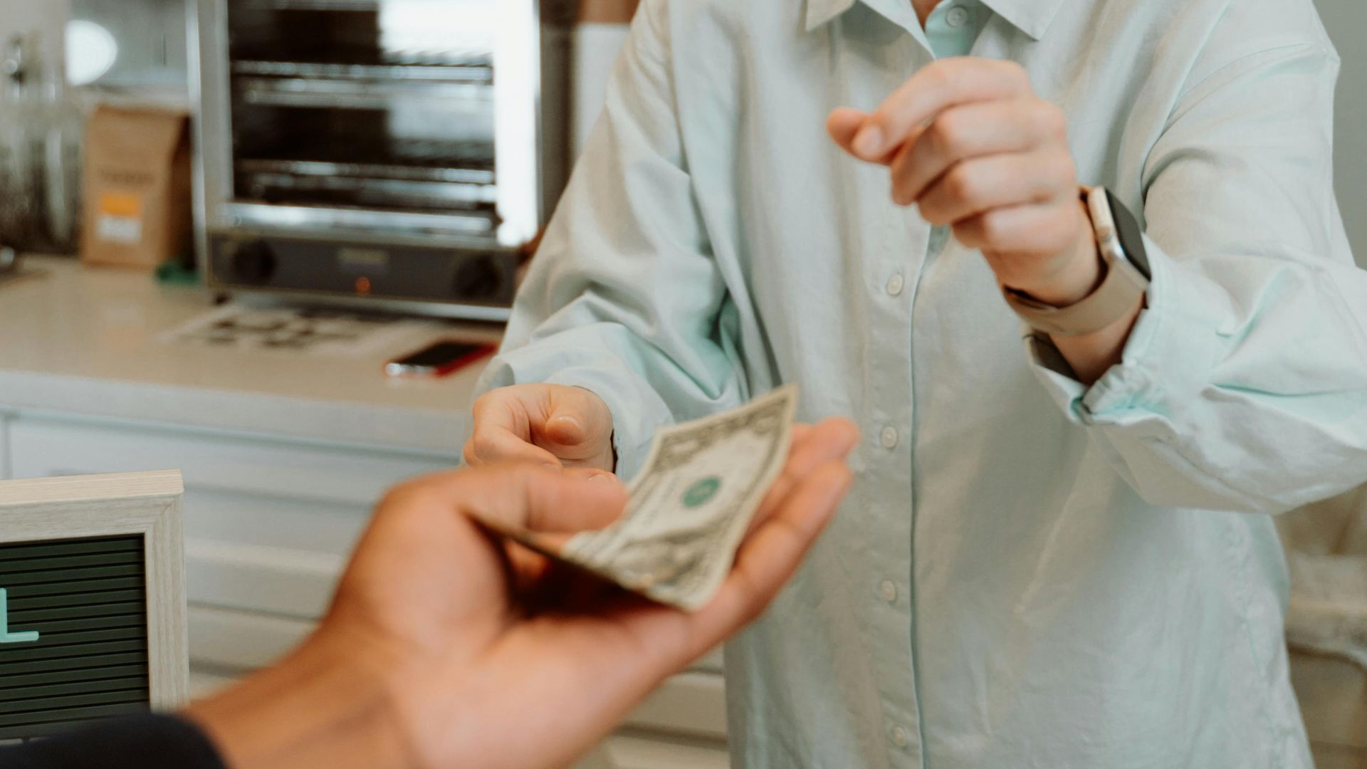 A cheerful barista receiving cash from a customer at a modern cafe counter, promoting a welcoming atmosphere.
