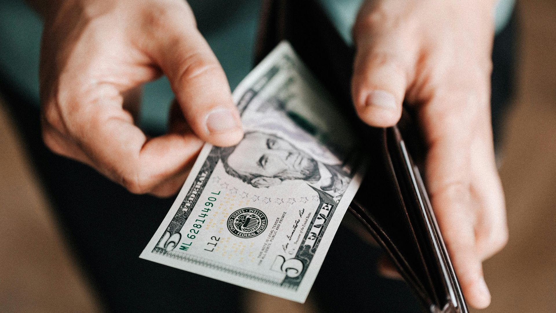 A person taking a five dollar bill from a wallet symbolizing personal finance and budget management.