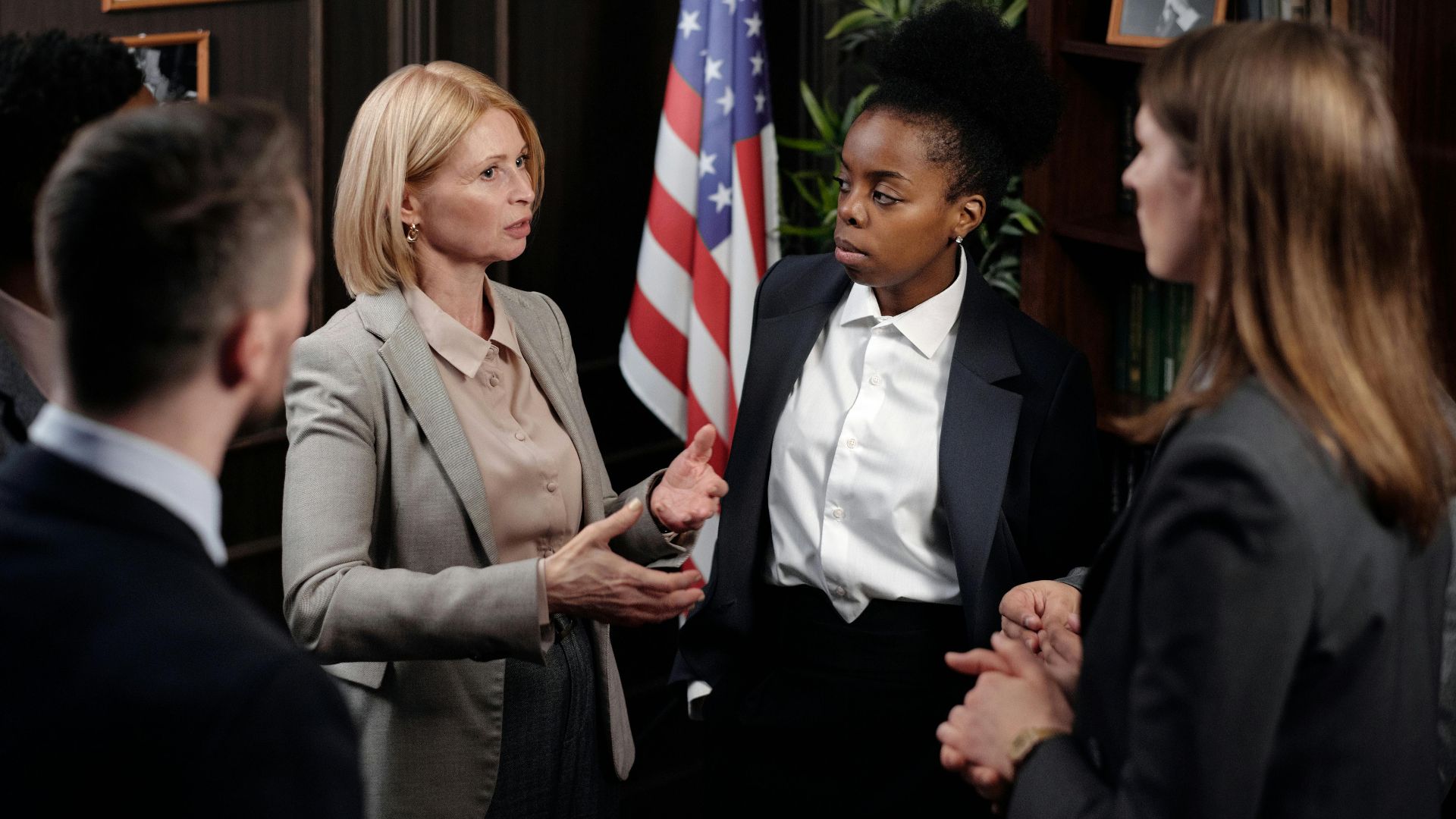 Diverse group of professionals in a discussion in a formal setting with an American flag.