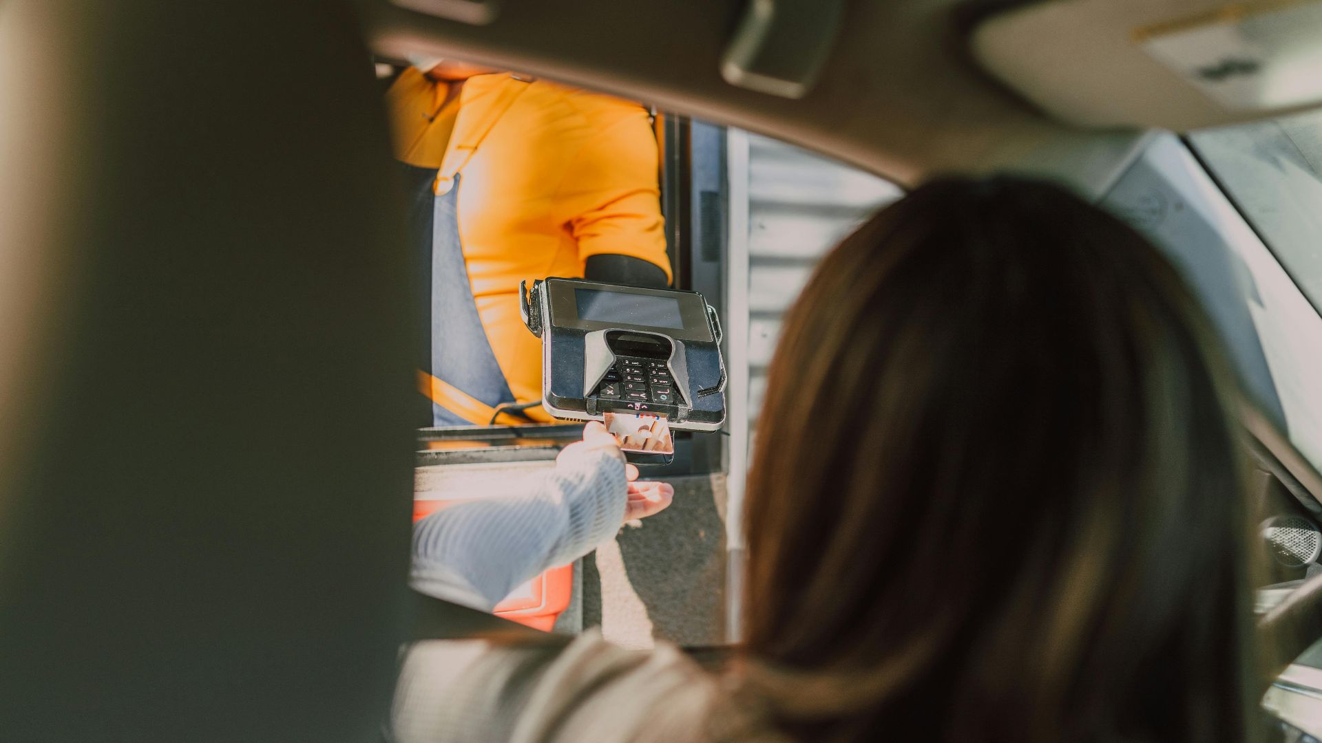 Customer makes a contactless payment at a fast-food drive-thru from a car.