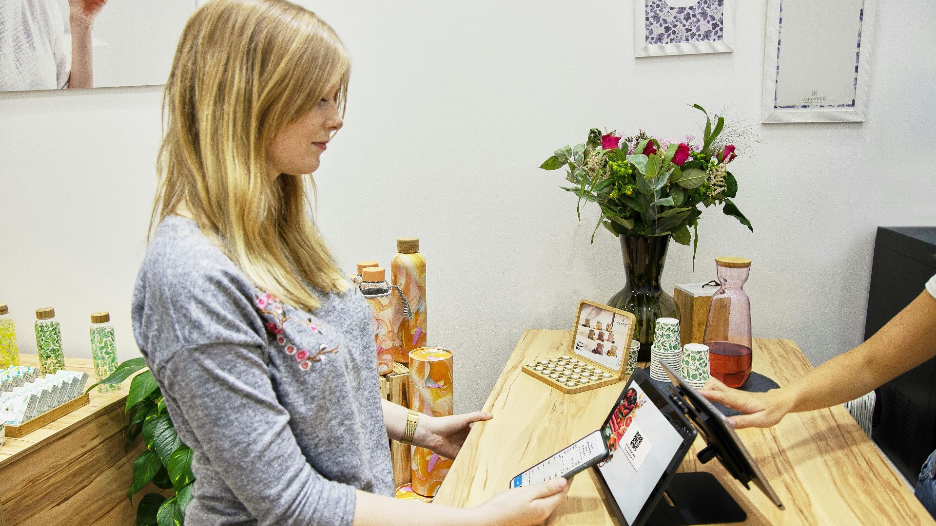 A woman uses a tablet to make a payment in a stylish Berlin store, featuring modern decor and eco-friendly products.