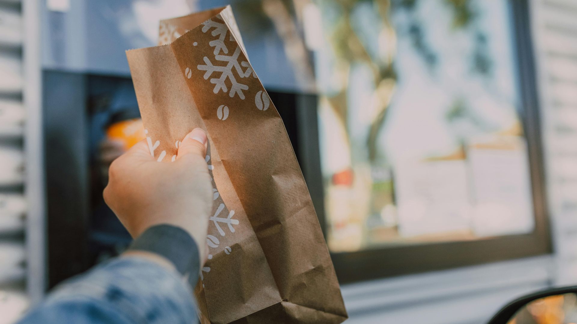Hand reaching out with brown paper bag at drive-thru window, showcasing casual takeout.