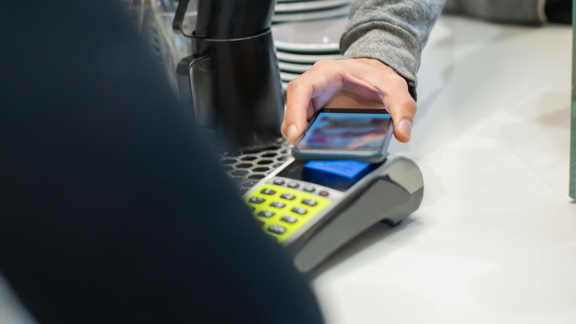 A customer makes a contactless payment using a smartphone at a café, showcasing modern digital transactions.