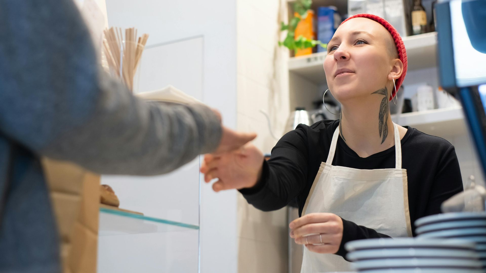 Barista with tattoos and red beanie serves a customer in a cozy Portugal café.