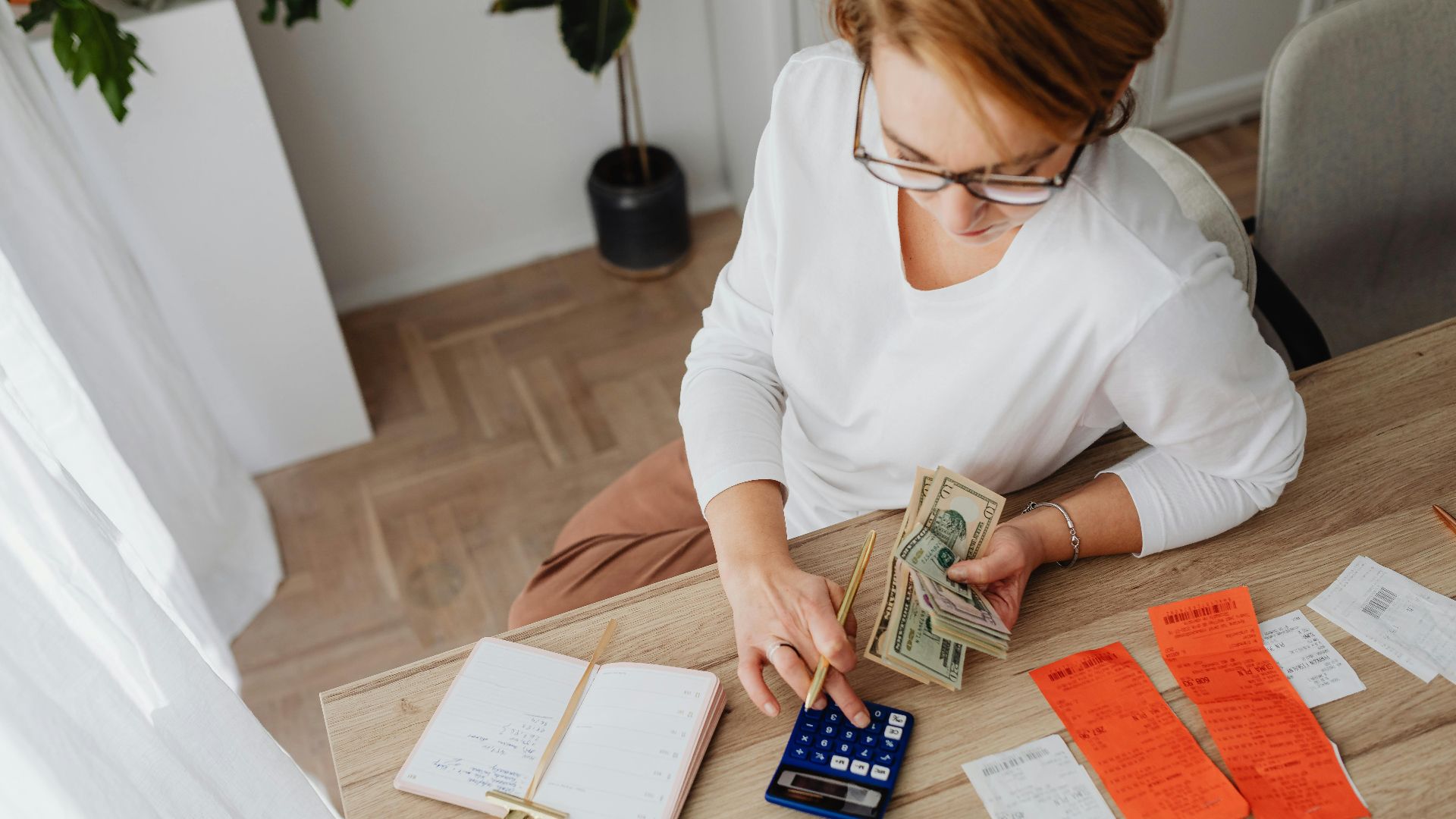 Top view of a woman managing finances with a calculator, cash, and bills in a home setting.