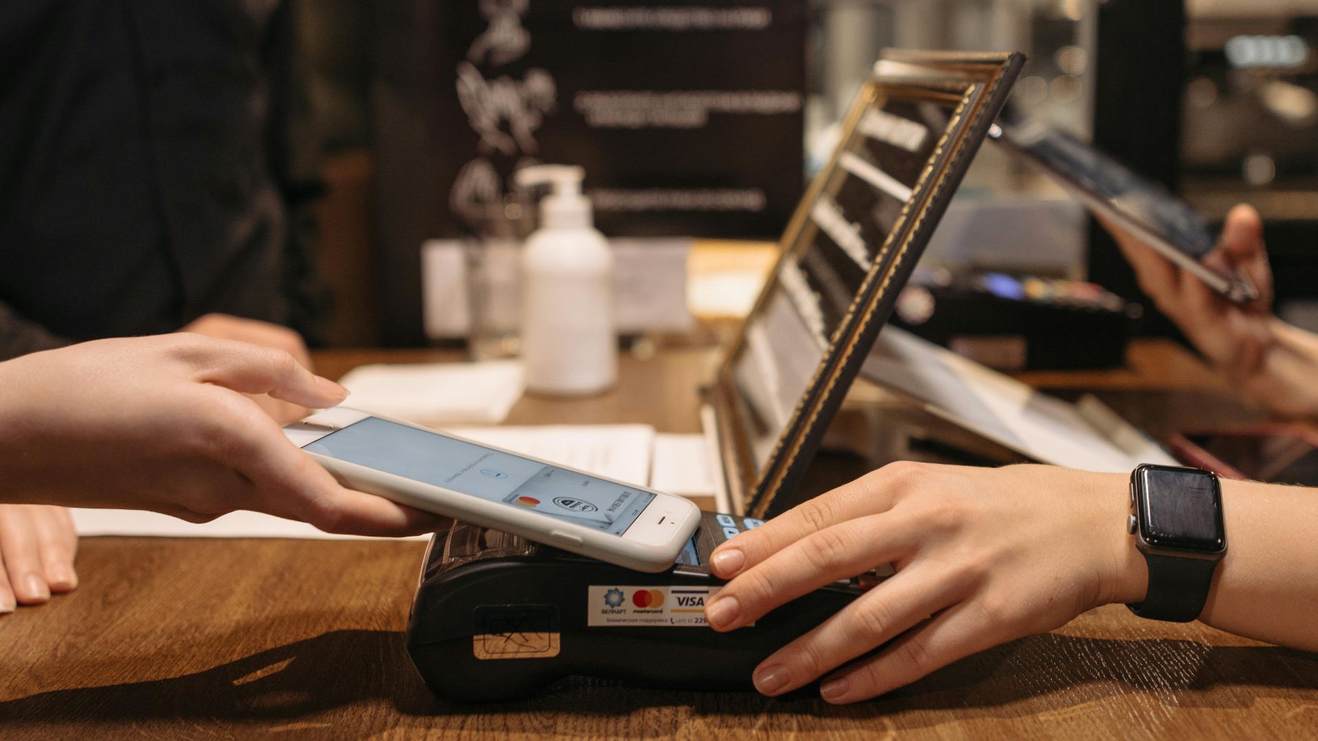 Hands using mobile for contactless payment at café terminal.