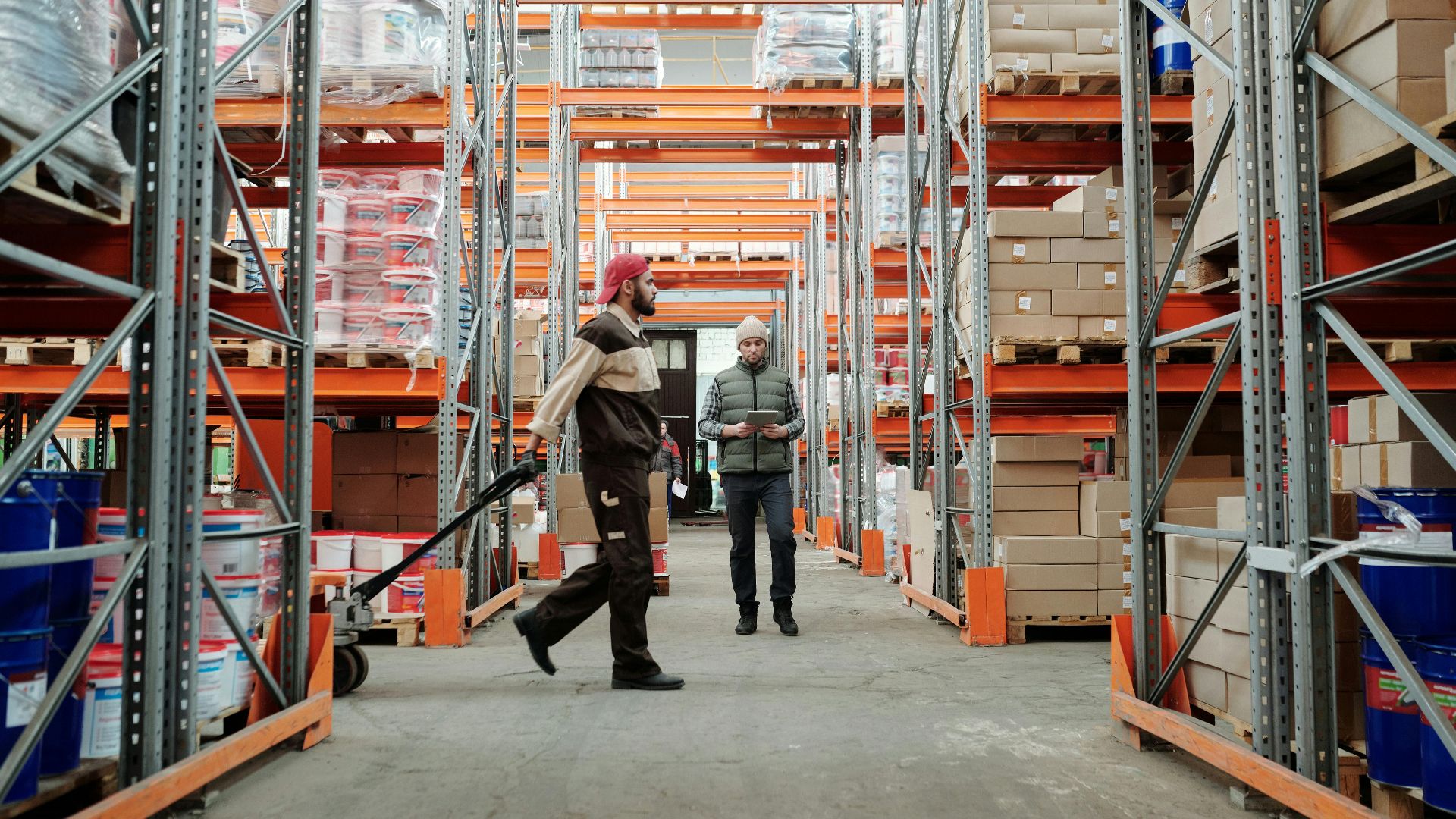 Two workers manage inventory in a spacious warehouse aisle.
