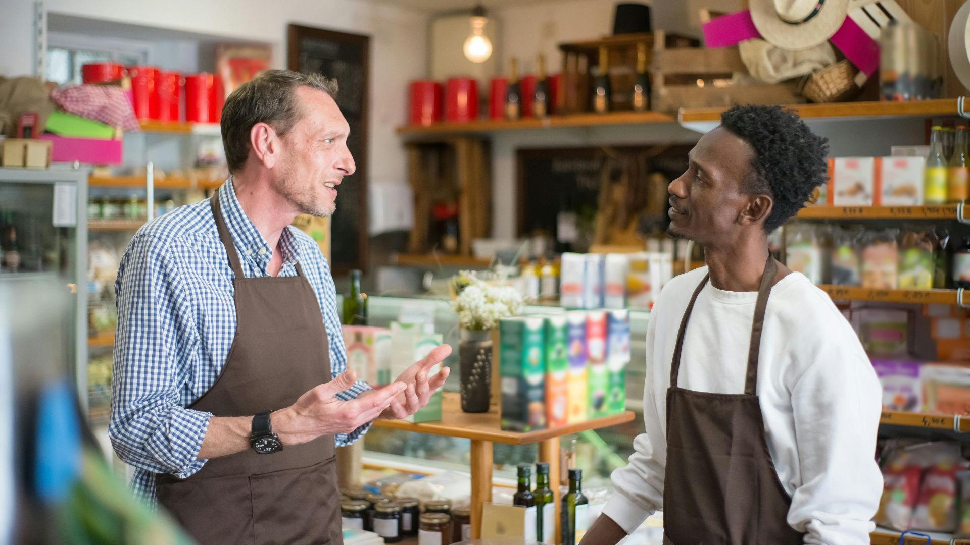 Two colleagues in aprons conversing in a grocery store setting.