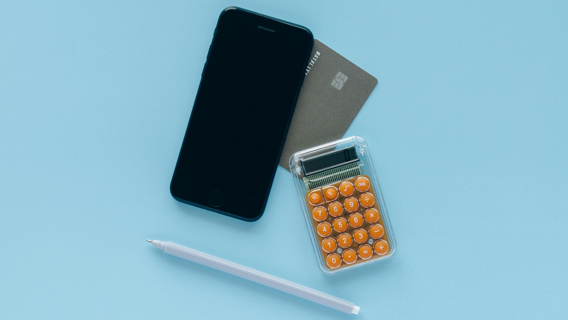 A modern flat lay of a smartphone, credit card, and calculator on a blue background.