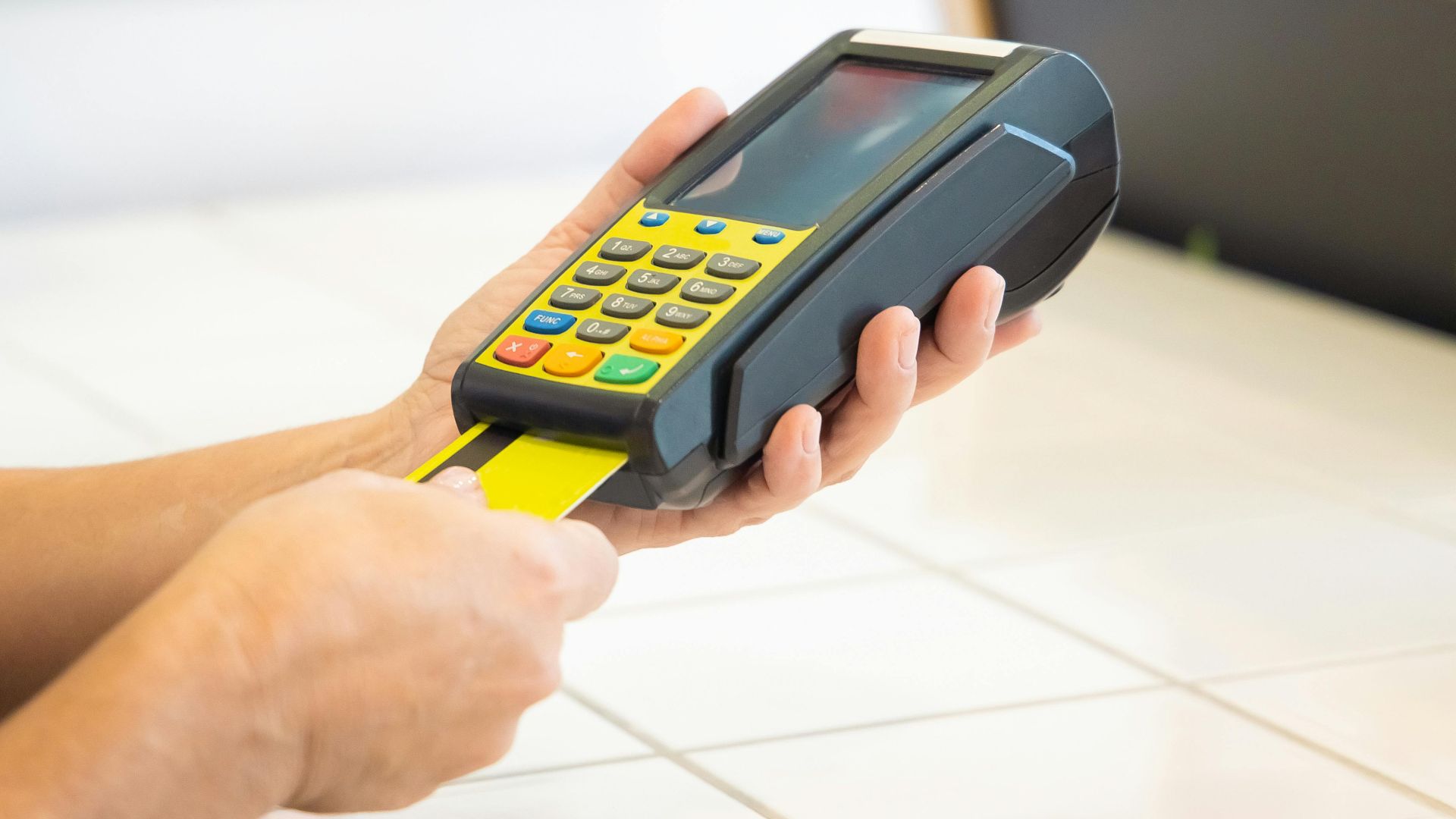Close-up of hands operating a credit card POS machine in a commercial setting.
