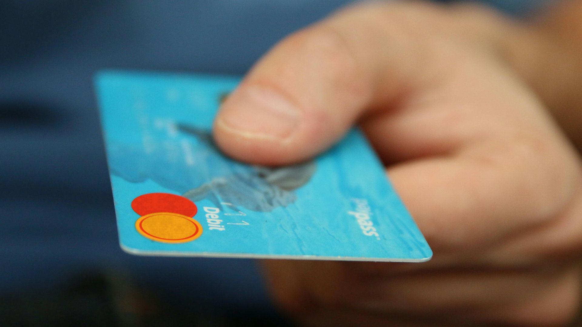 A close-up shot of a hand offering a blue debit card for payment.