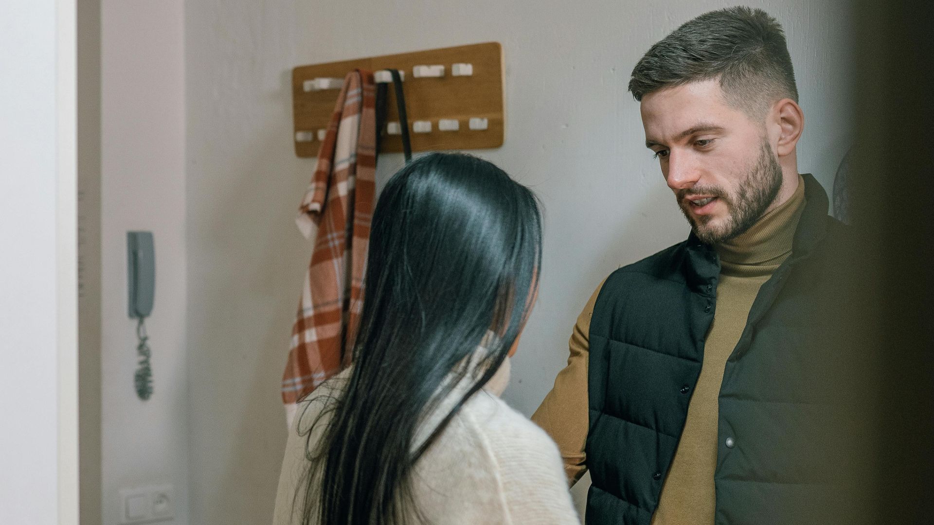 A man and woman talk inside a cozy home. They appear engaged in a conversation.