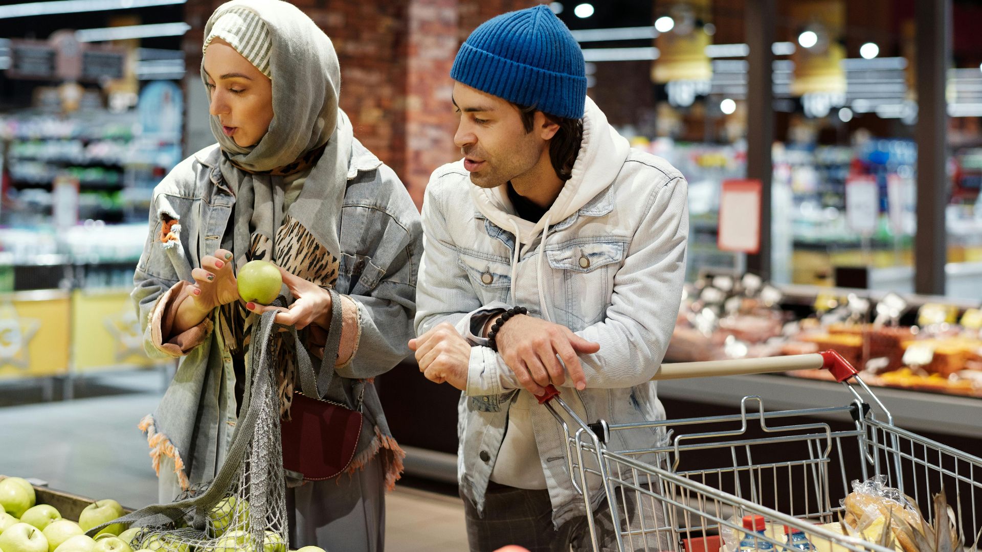 A Middle Eastern couple shopping for apples at a supermarket, engaging in conversation.