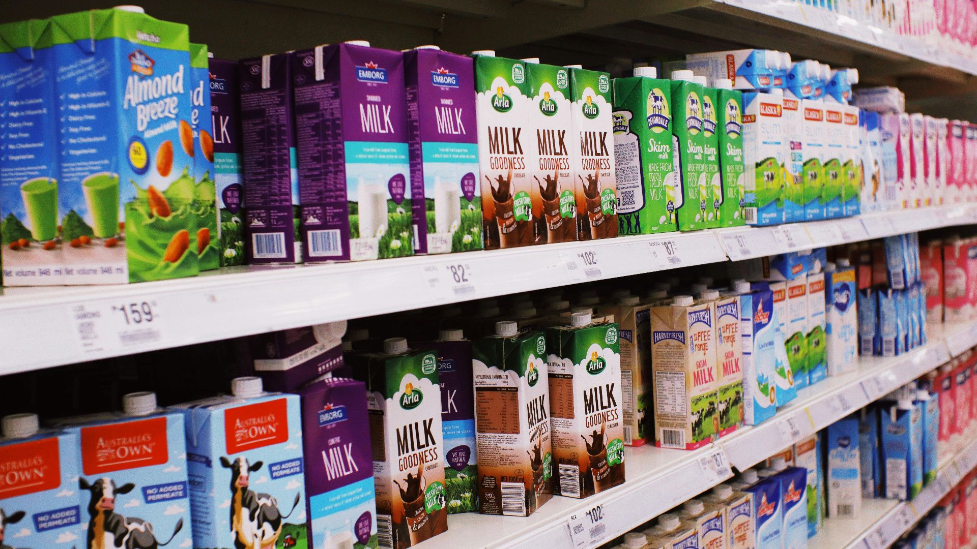Various milk cartons displayed on shelves in a bright supermarket aisle.