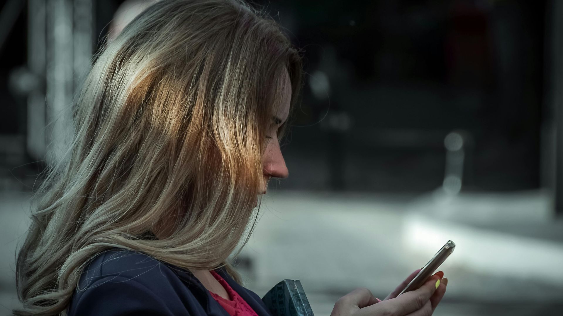 Side profile of a young woman texting on her smartphone in a shaded outdoor area.