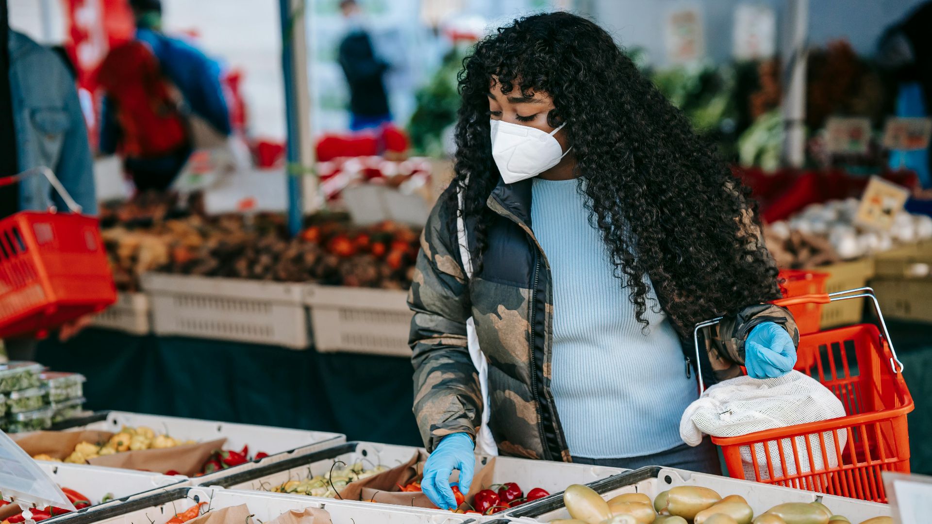 A woman wearing a face mask selects fresh produce at an outdoor market.