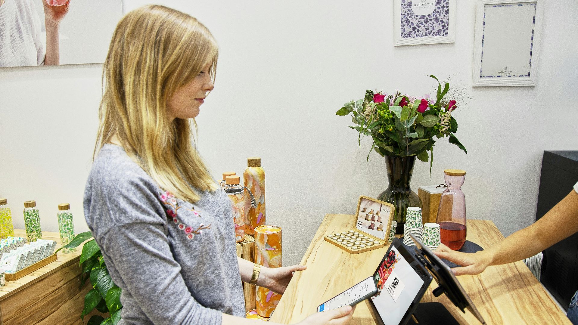 A woman uses a tablet to make a payment in a stylish Berlin store, featuring modern decor and eco-friendly products.