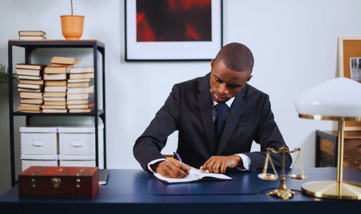 A Man in a Suit Writing on a Notebook in His Office