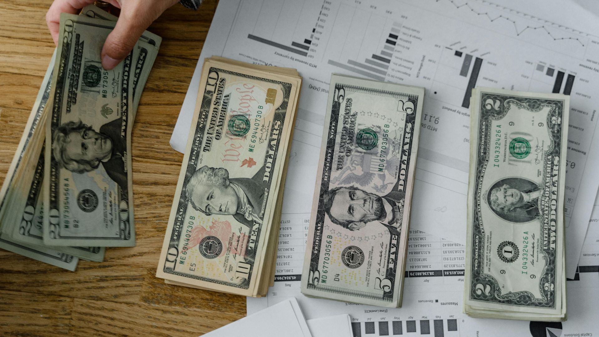 Person holds US dollars over financial papers, showing income or budget analysis.