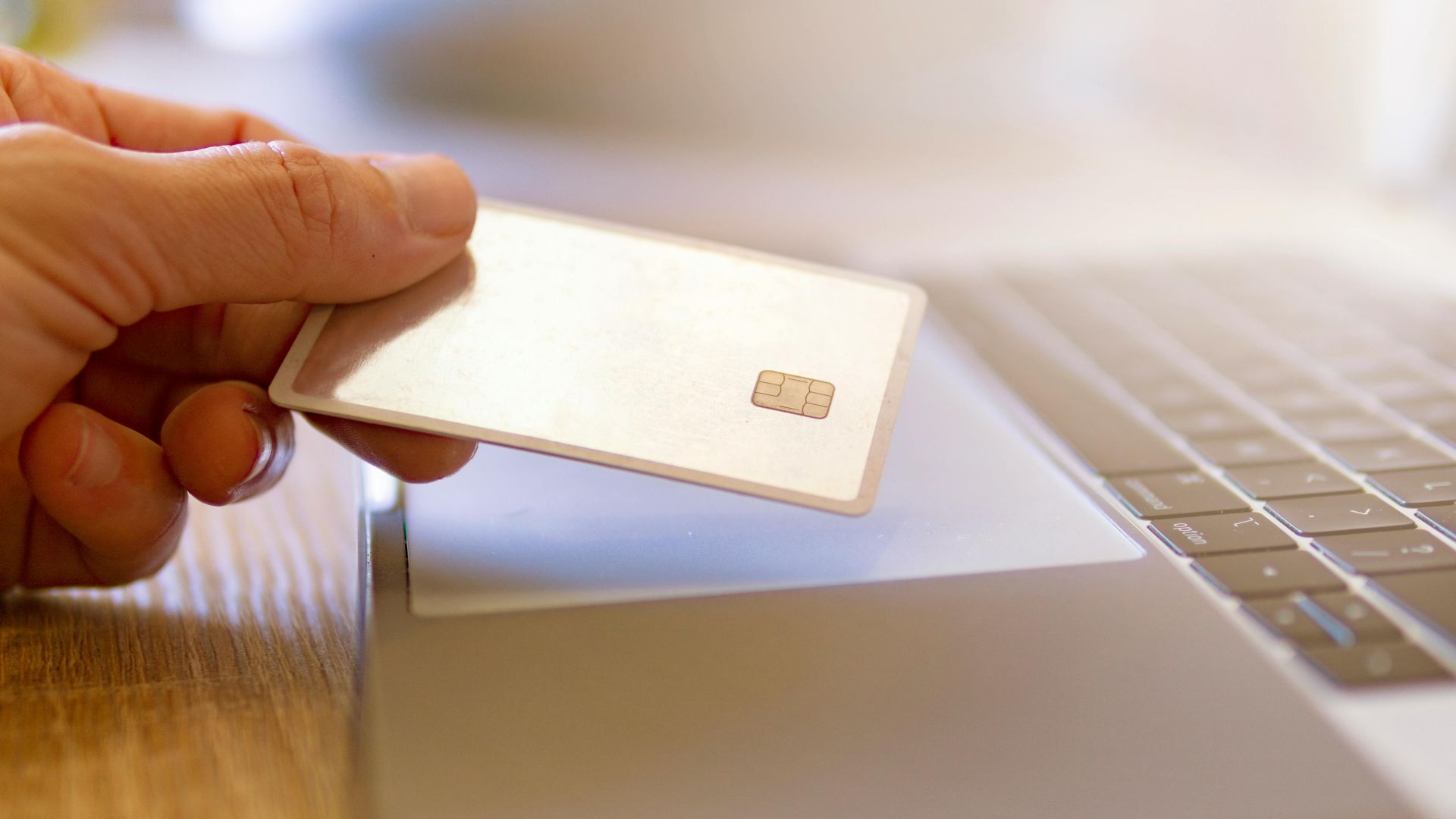A person holds a credit card near a laptop for online shopping.
