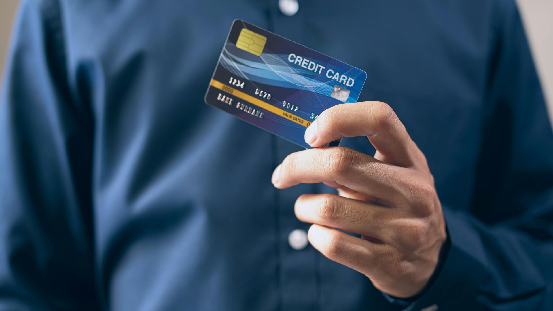 Close-up of a person holding a credit card in a hand, wearing a button-up shirt.
