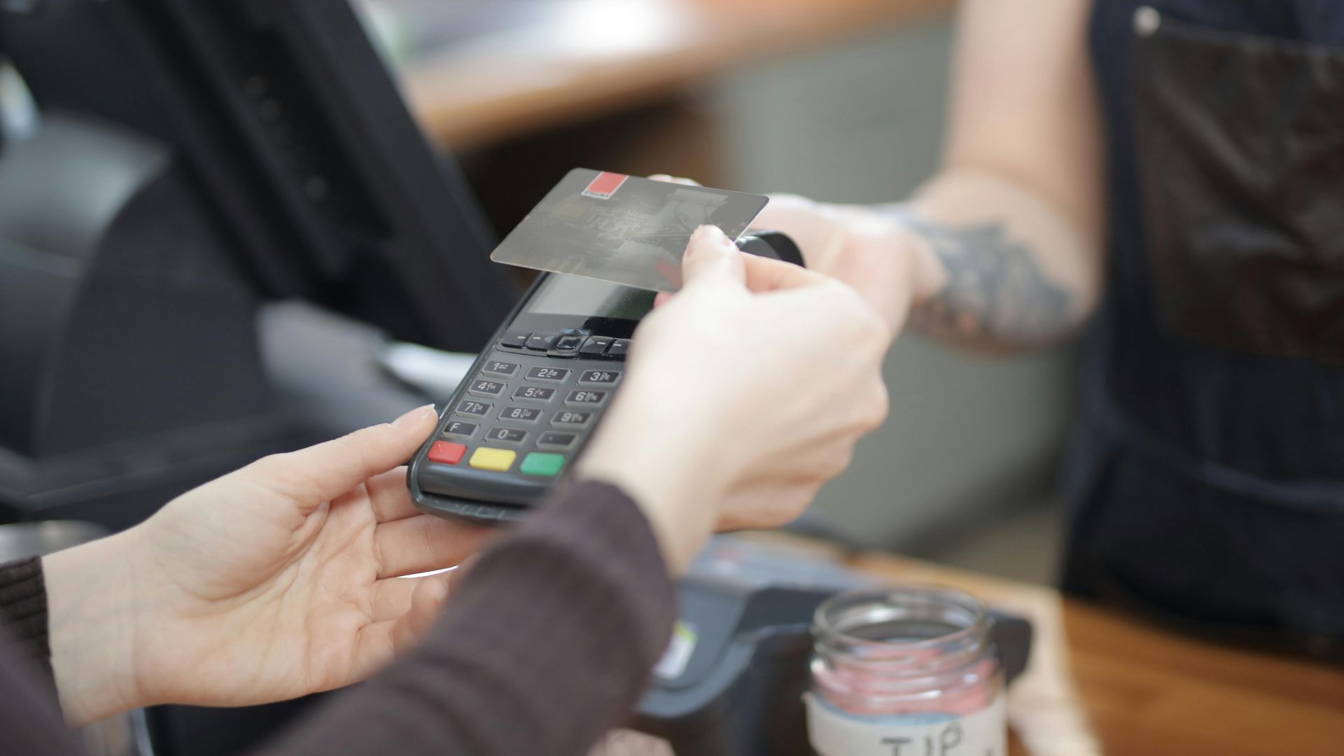 Close-up of customer and cashier during a credit card transaction at a store counter indoors.