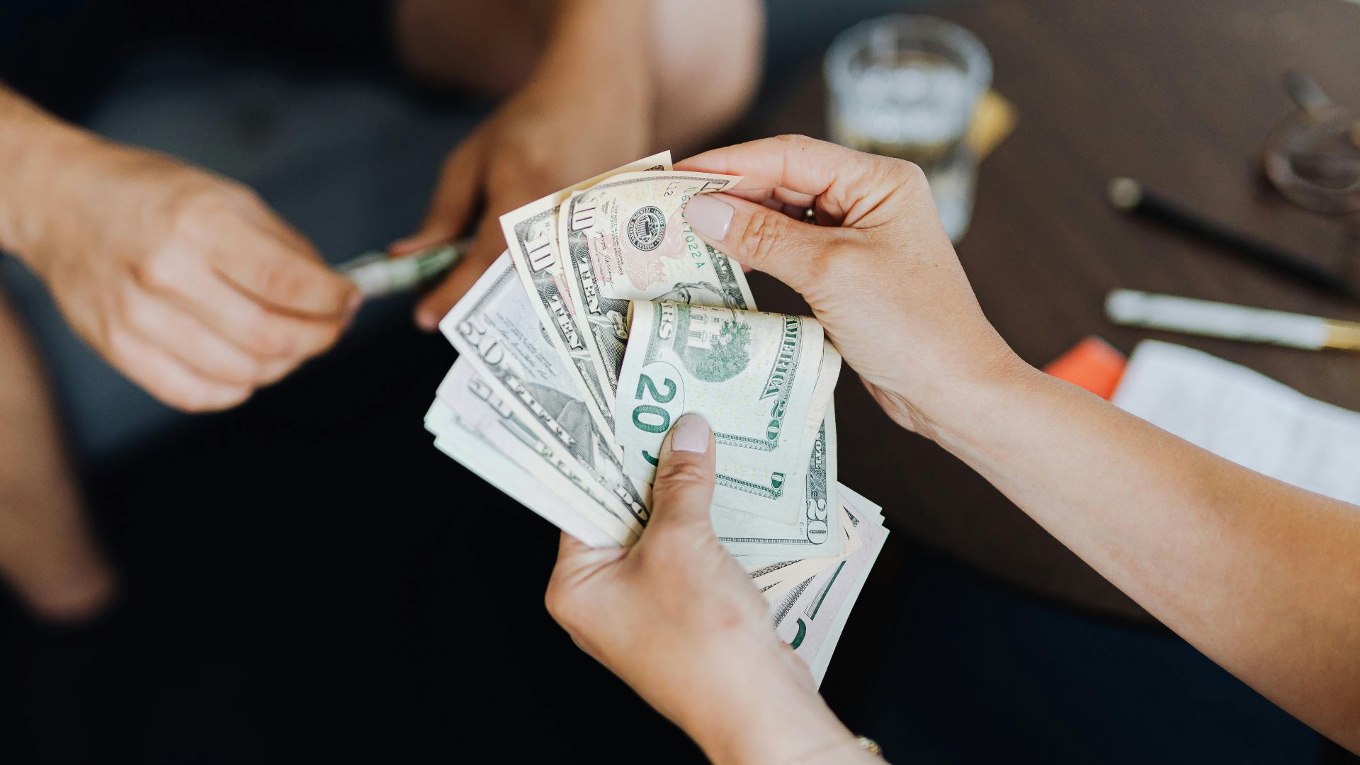 Close-up of people handling and counting US dollar bills indoors.