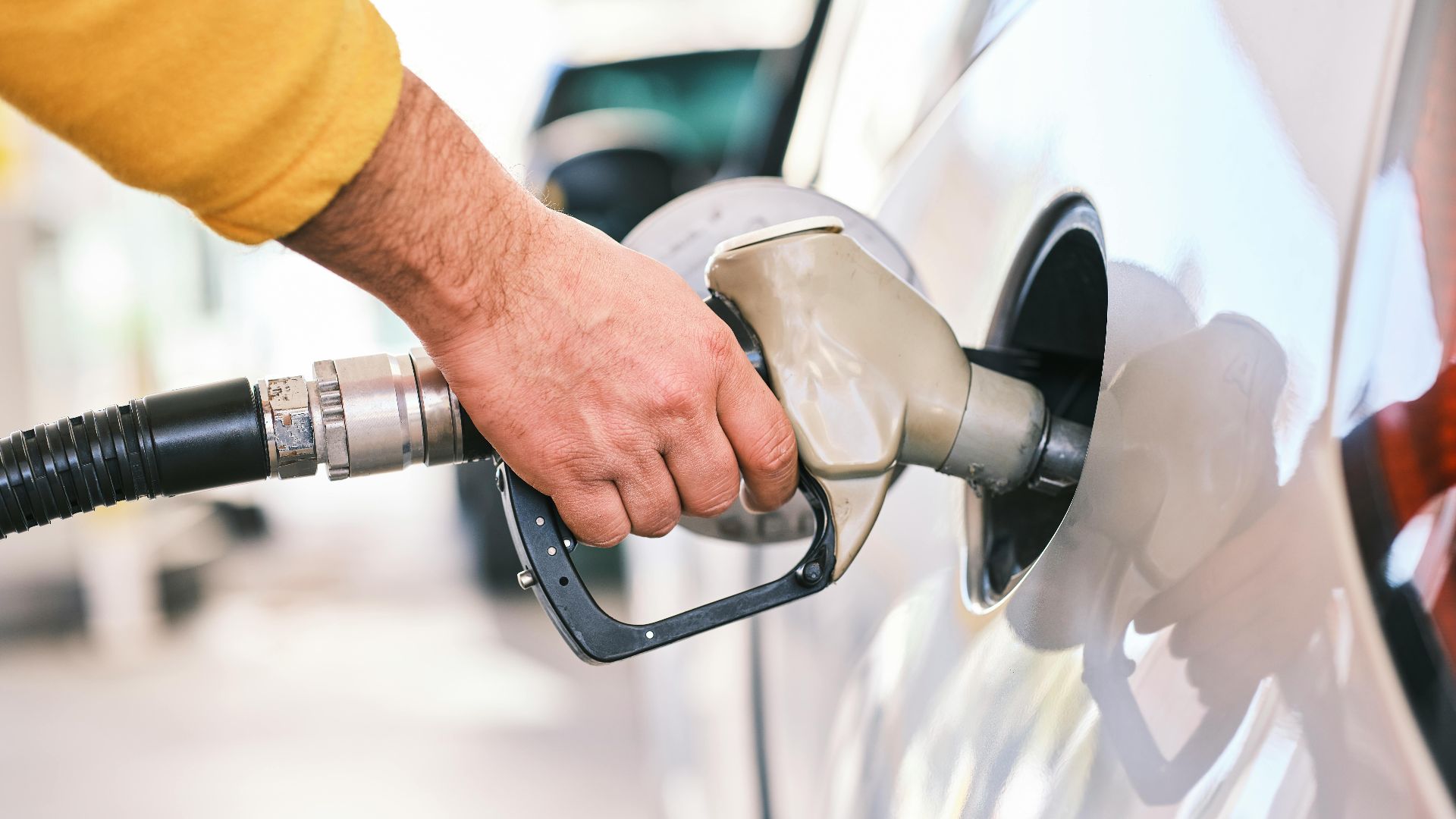 Close-up of a person refueling a car with a gas nozzle at a station.