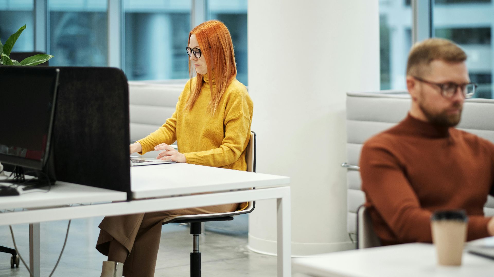 Two professionals working in a contemporary office environment with computers and casual attire.
