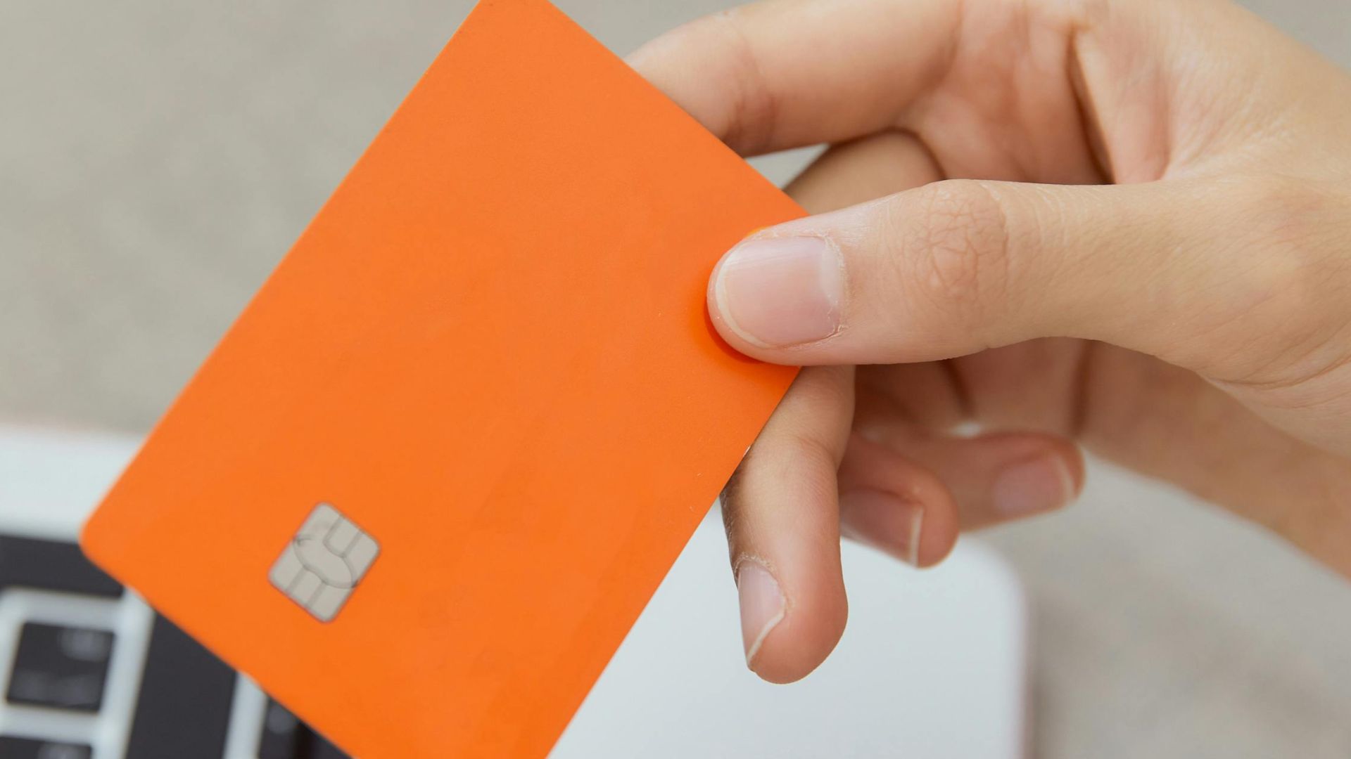 Close-up shot of an orange credit card held above a laptop, emphasizing digital payment.