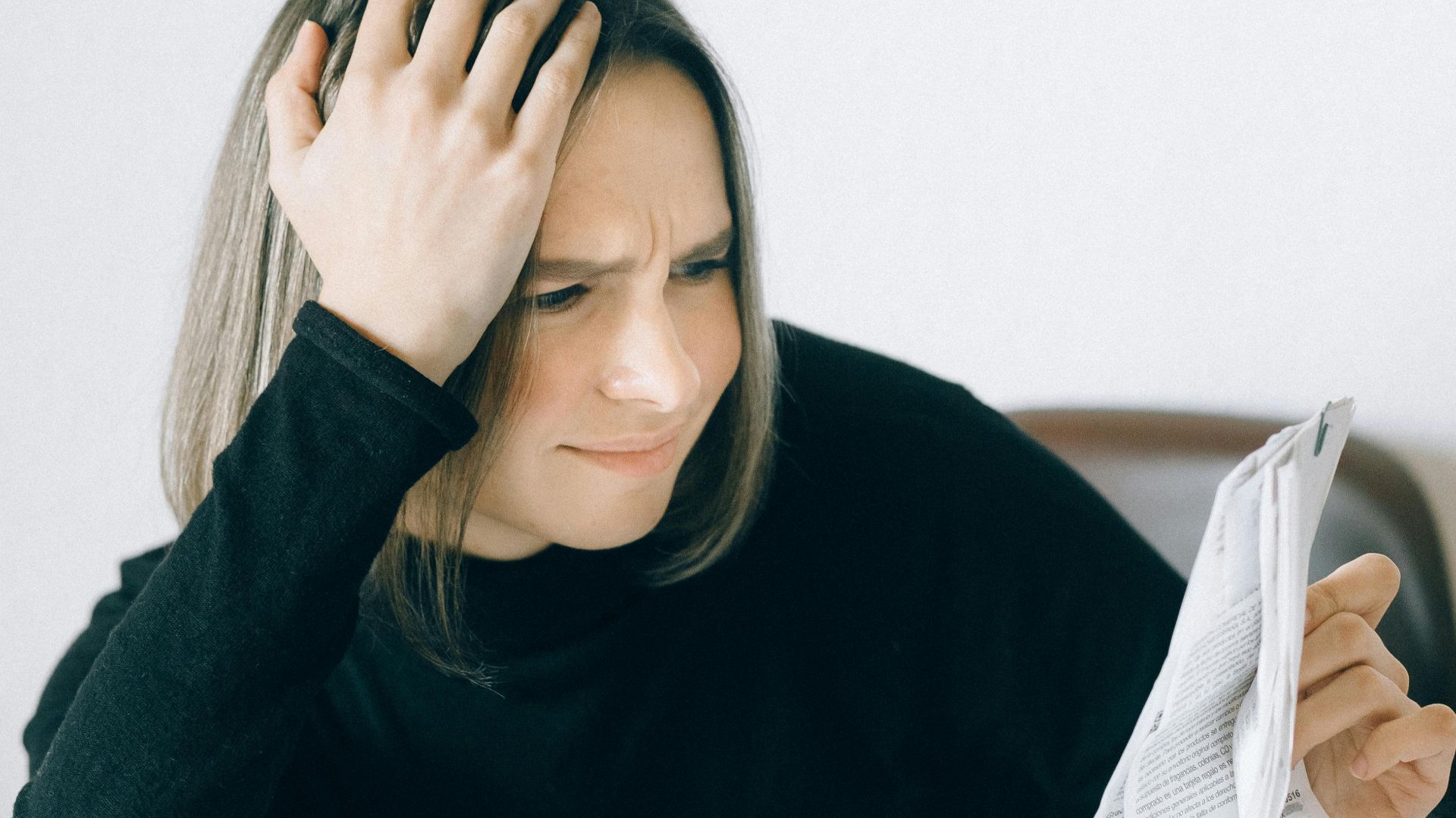 A woman looking concerned while analyzing financial papers at a desk, representing work stress.