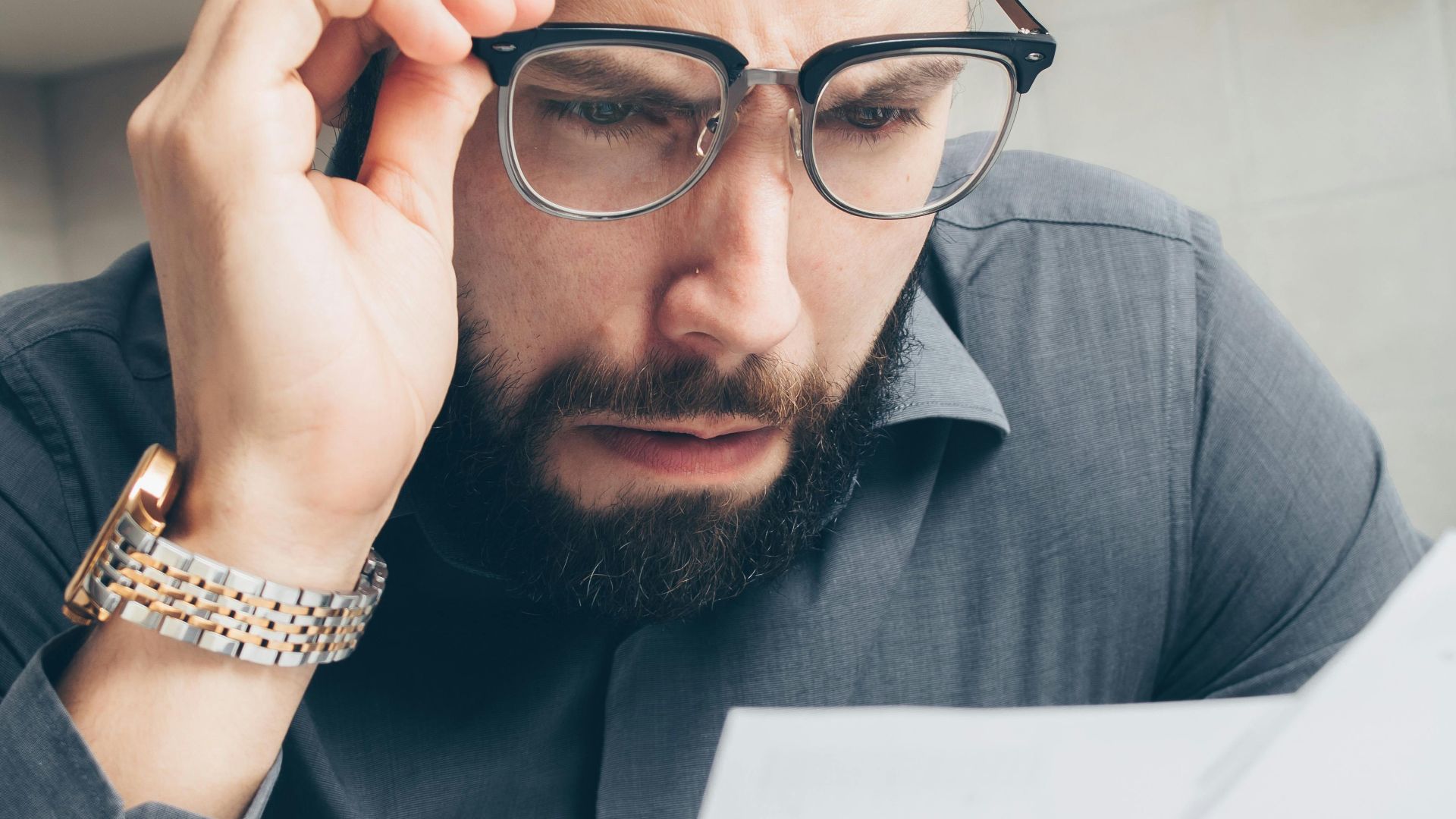 Man with glasses scrutinizing financial papers, showing concern.
