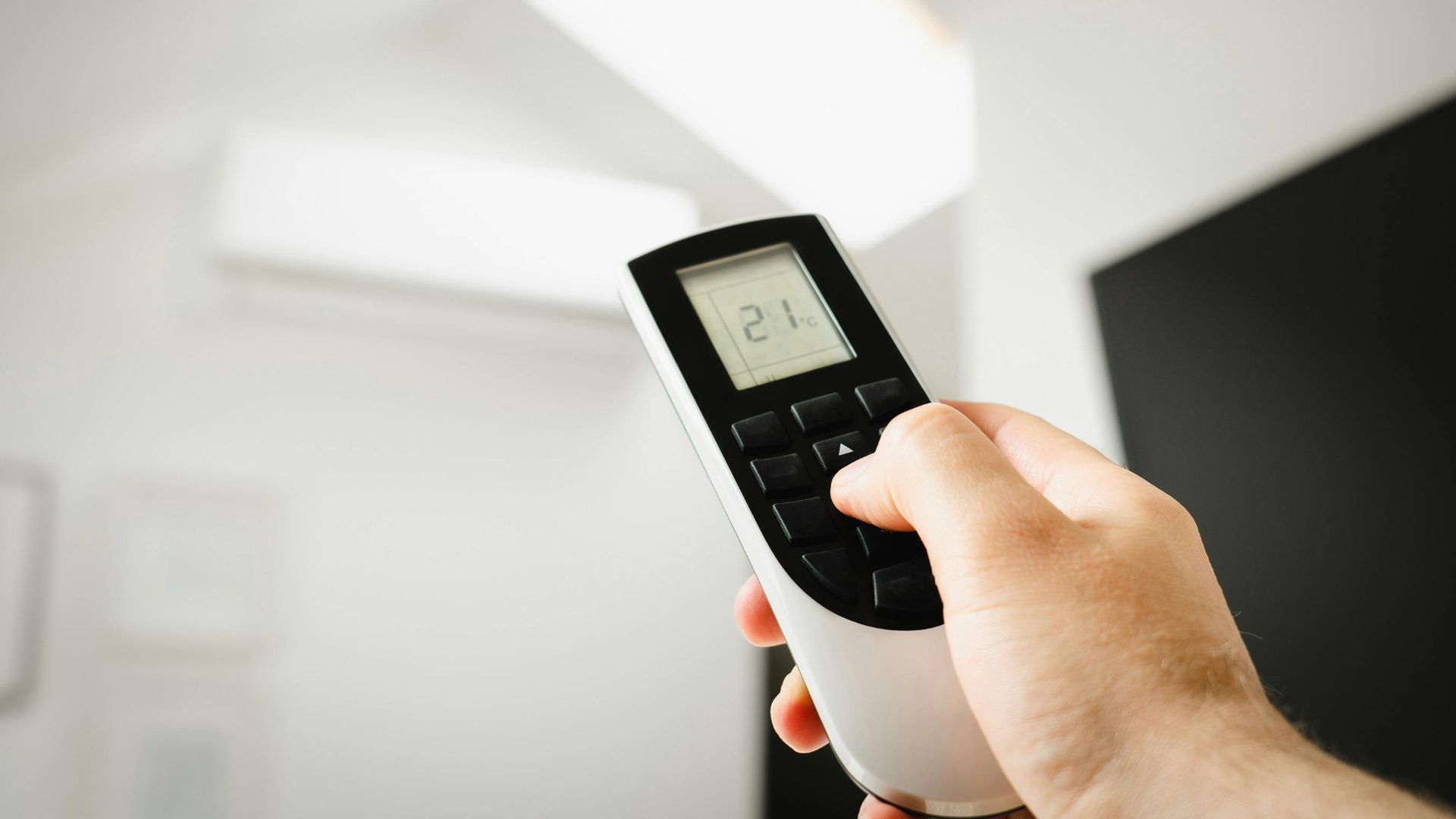Close-up of a man using a remote to control air conditioning indoors.