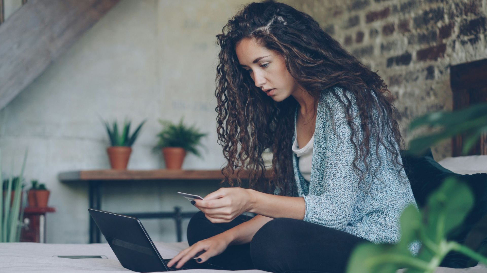 Woman using laptop and credit card on bed.