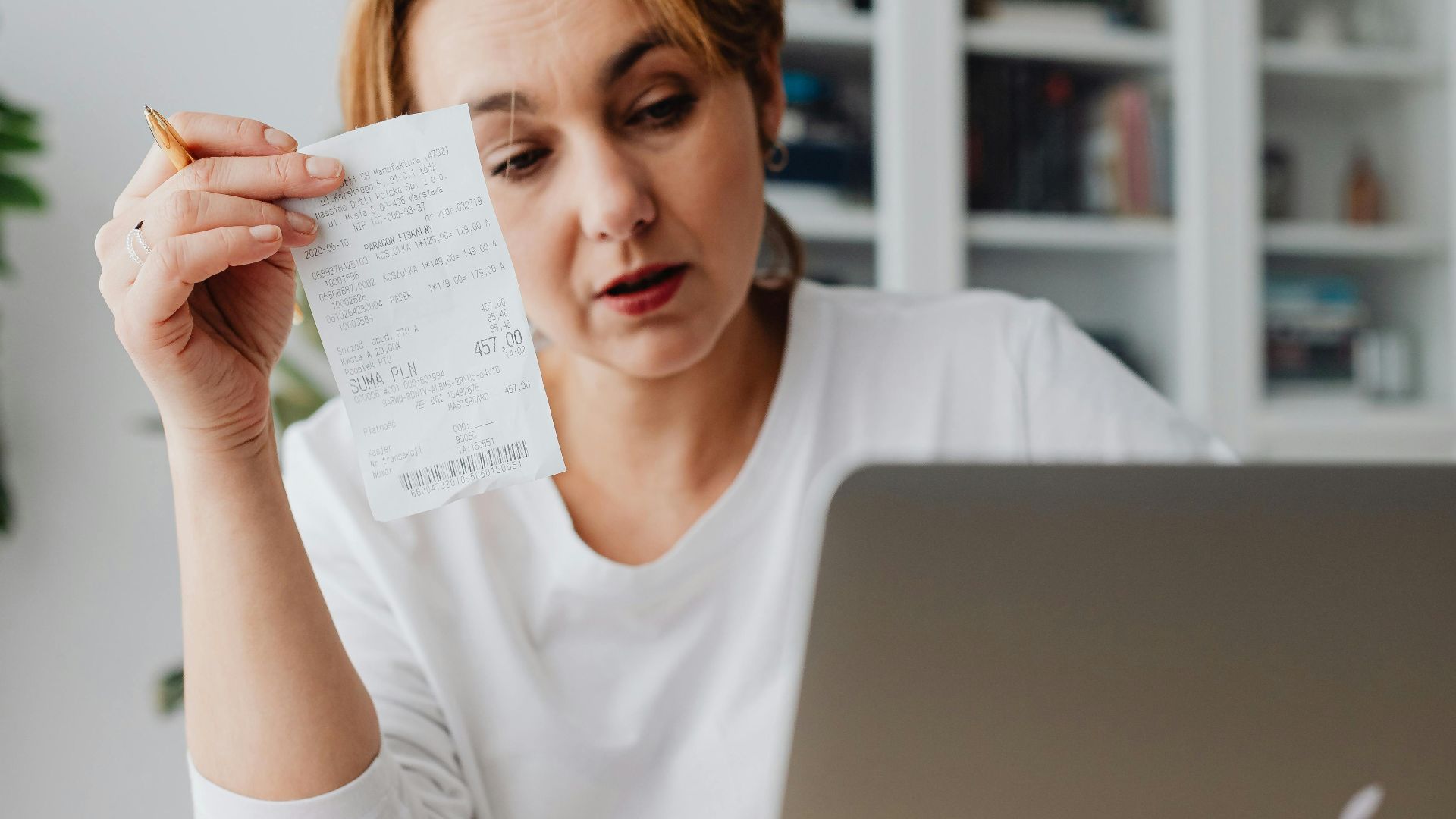 Woman using laptop while managing finances with receipts and cash on the table.