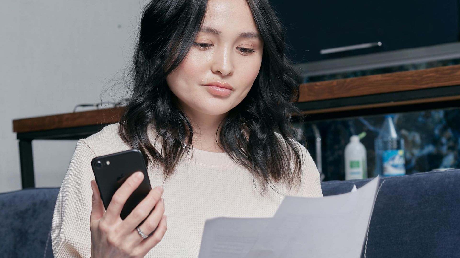 Young woman using phone and documents for home finance management.
