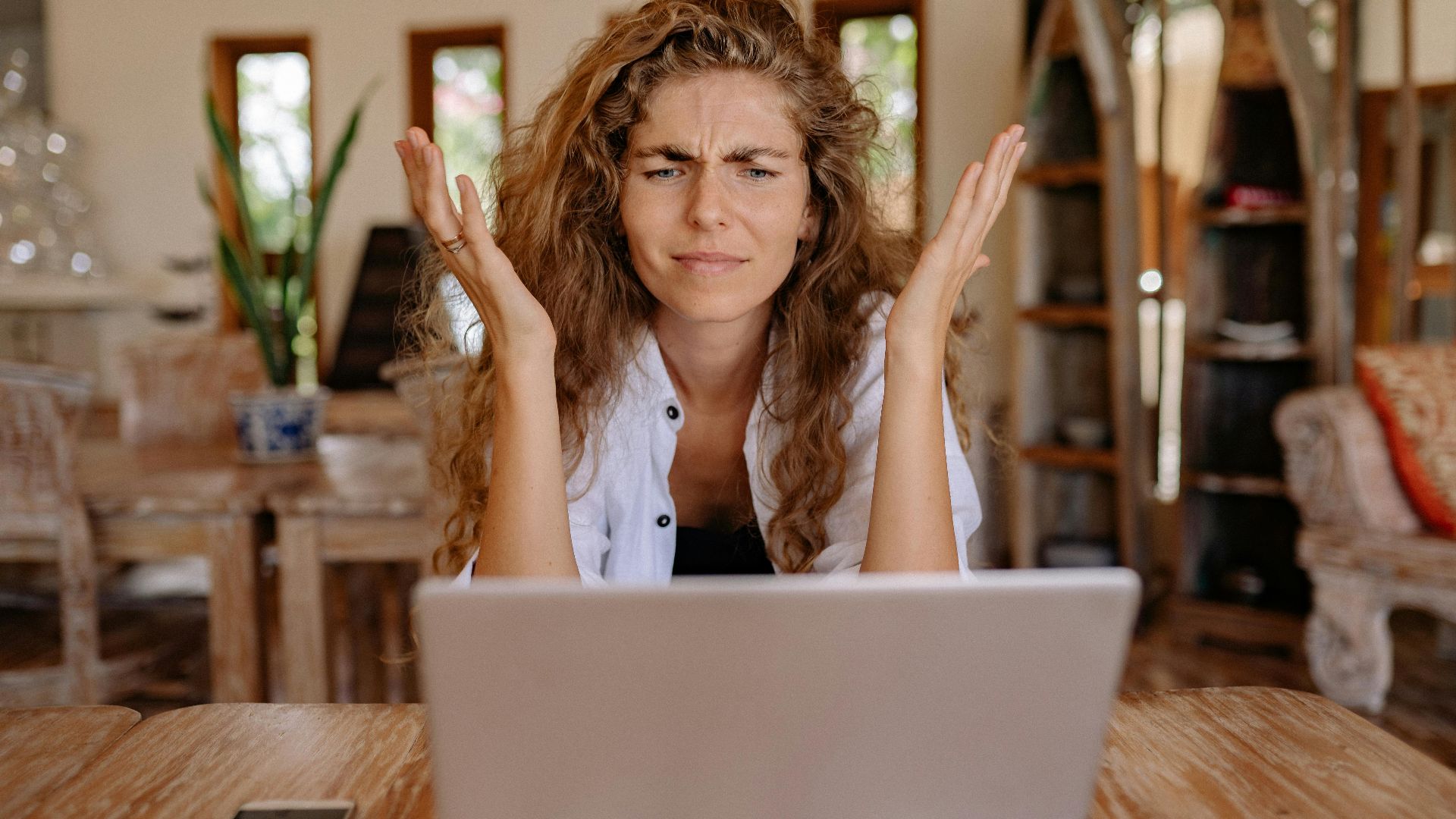 A woman frustrated with her laptop while working remotely indoors, expressing stress.