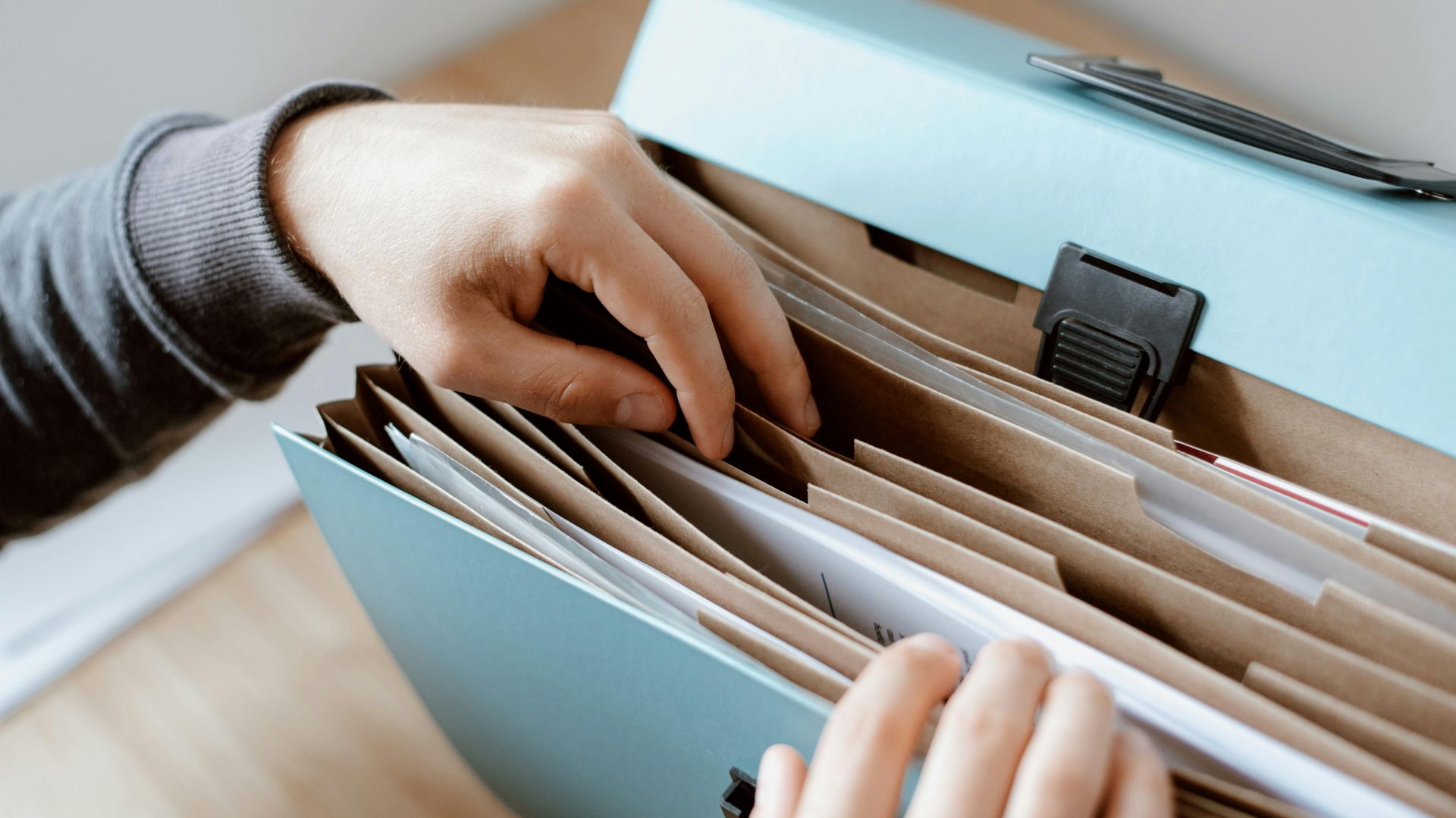 Close-up of hands organizing papers in a blue folder, ideal for business and office concepts.