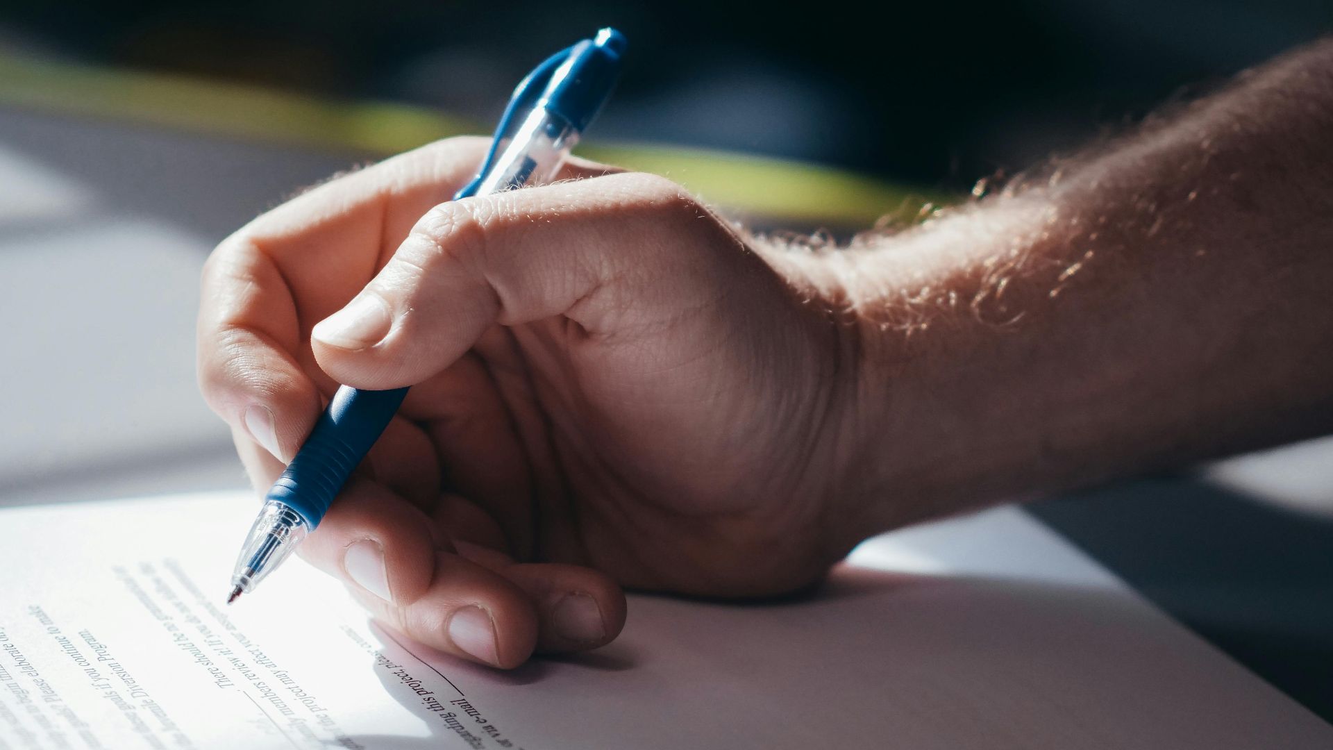 Detailed shot of a hand holding a blue pen while signing a document. Ideal for legal and business themes.