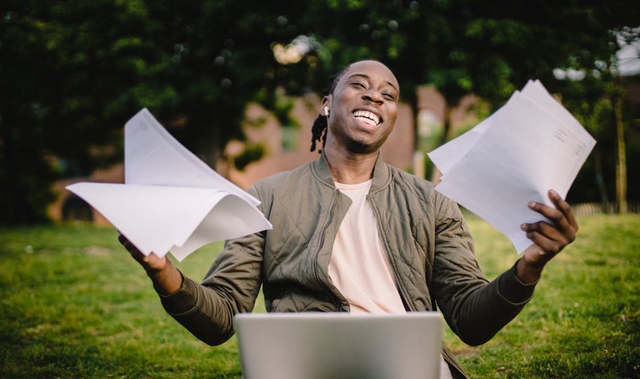 Happy African American man holding sheets of paper in front of laptop