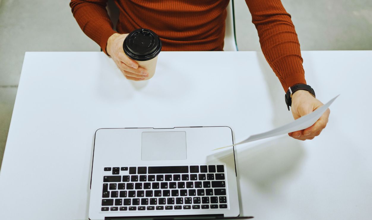 Man Holding Disposable Cup, and Sitting at Desk