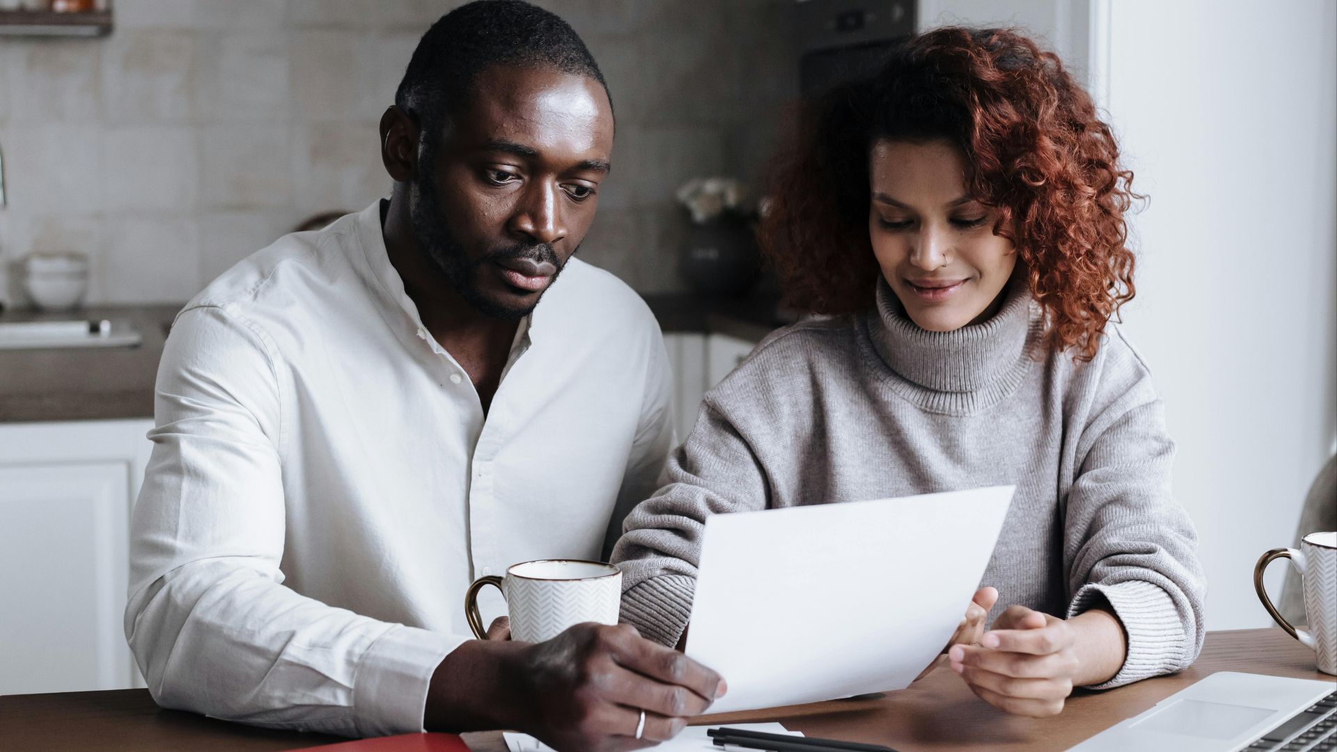 A couple reviews paperwork at a kitchen table, embodying teamwork and collaboration.