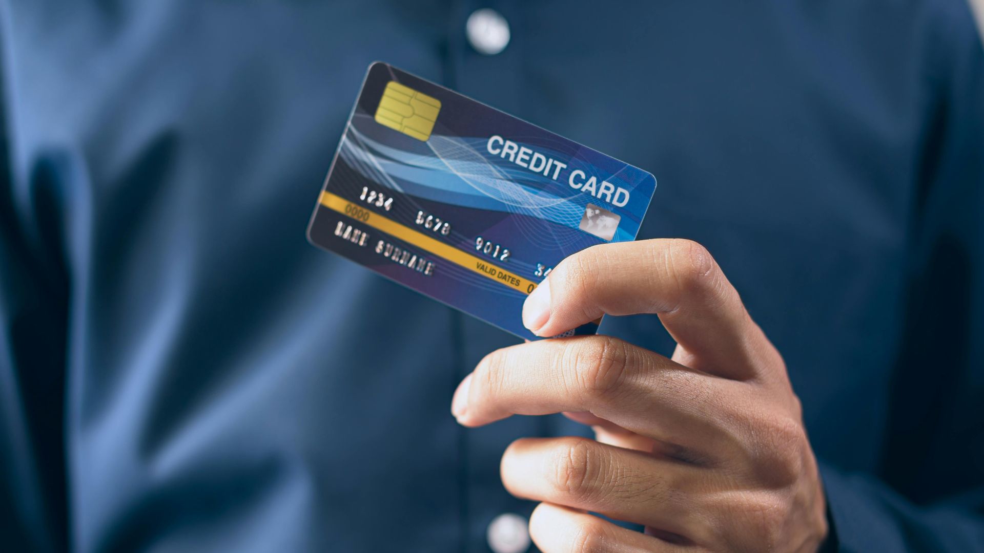 Close-up of a person holding a credit card in a hand, wearing a button-up shirt.
