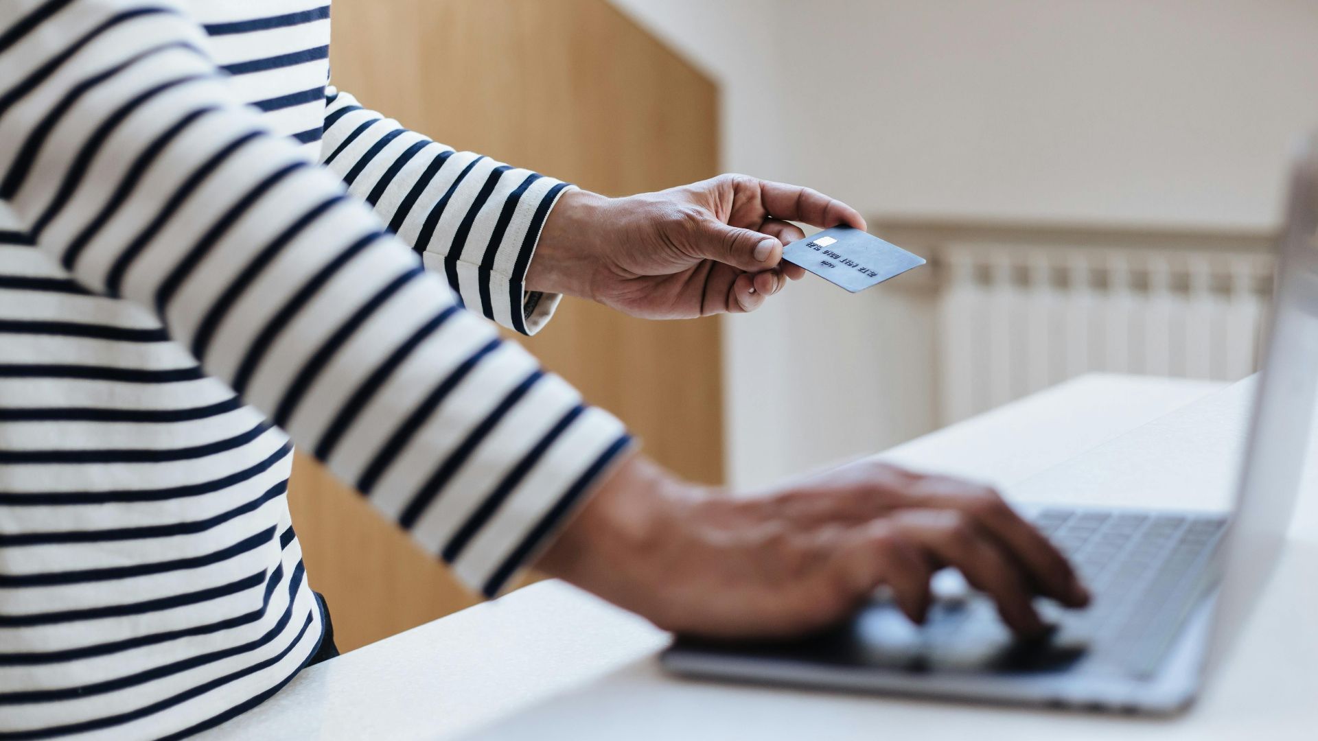 Person using a credit card for online shopping on a laptop indoors.