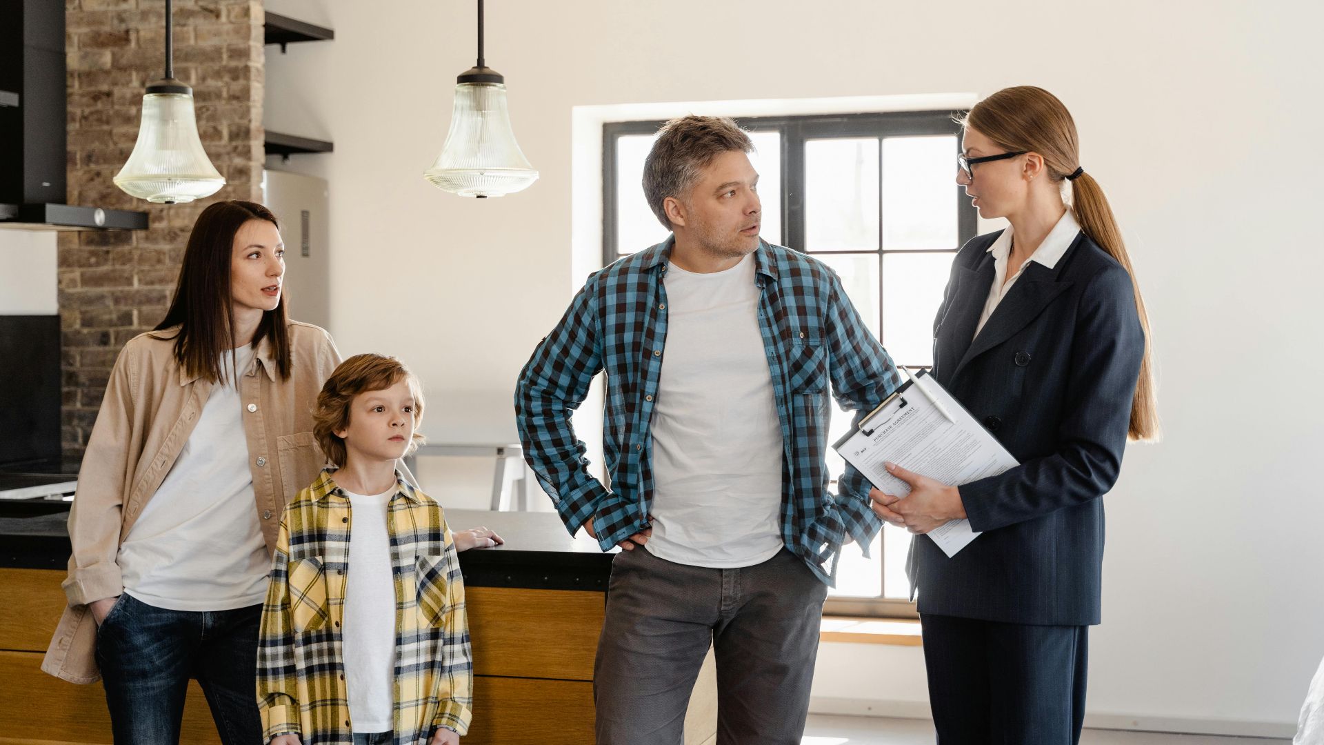Family with child talks to real estate agent in modern kitchen during home showing.