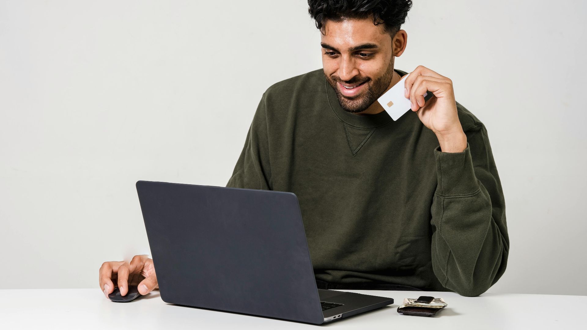 A man smiling while using a laptop and holding a credit card for online shopping.