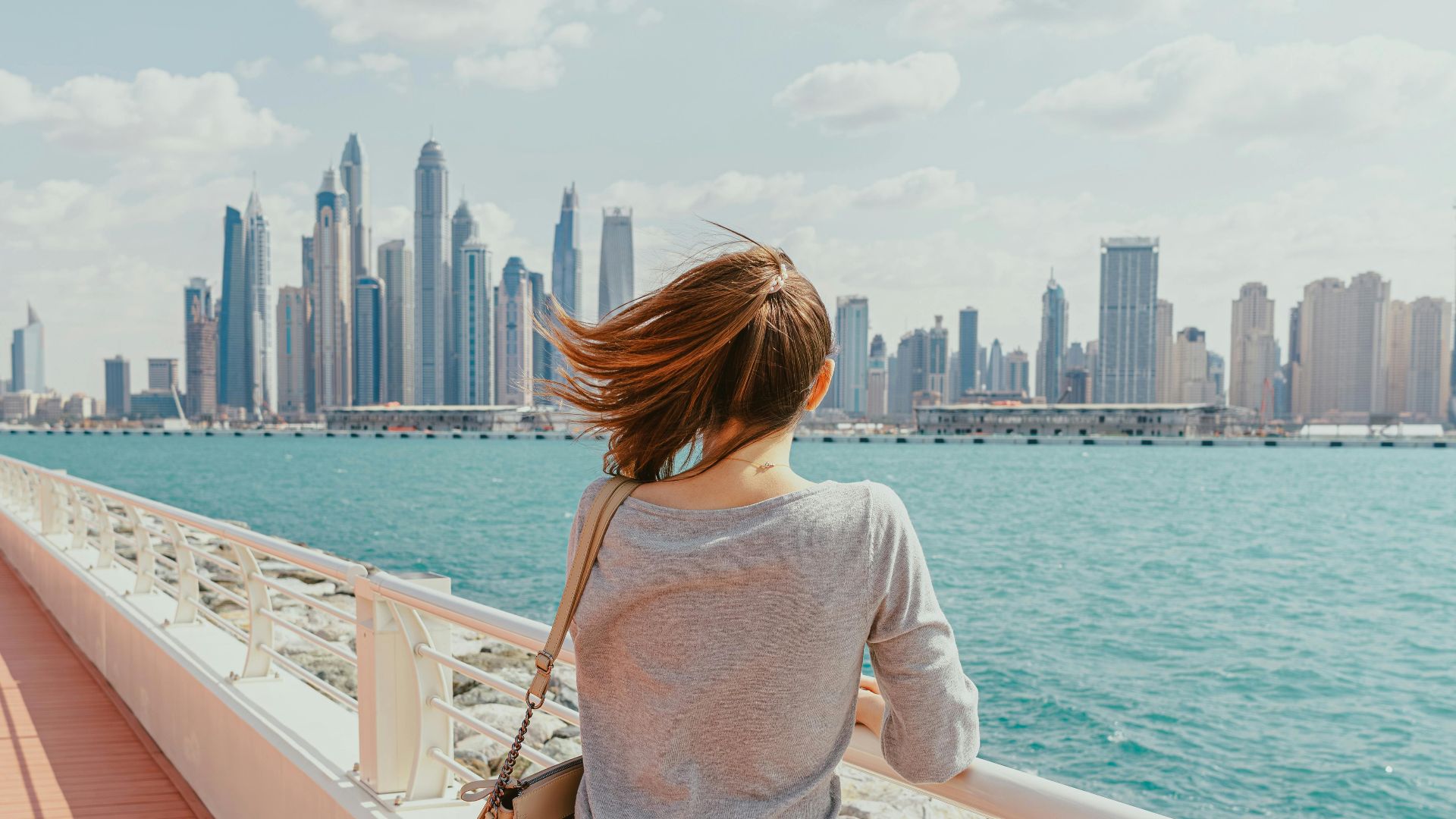 Woman gazes at Dubai Marina's modern skyline from a waterfront promenade.